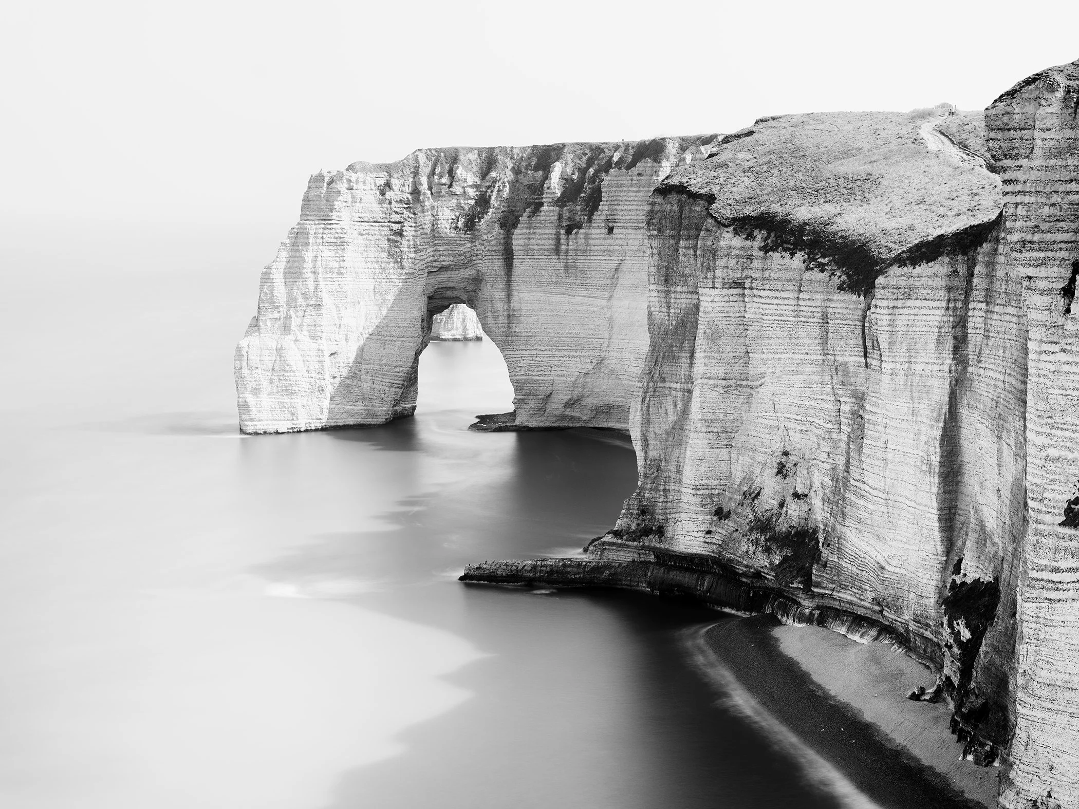 Black-and-white long-exposure photograph of Étretat’s chalk cliffs and sea arch on Normandy’s Alabaster Coast.