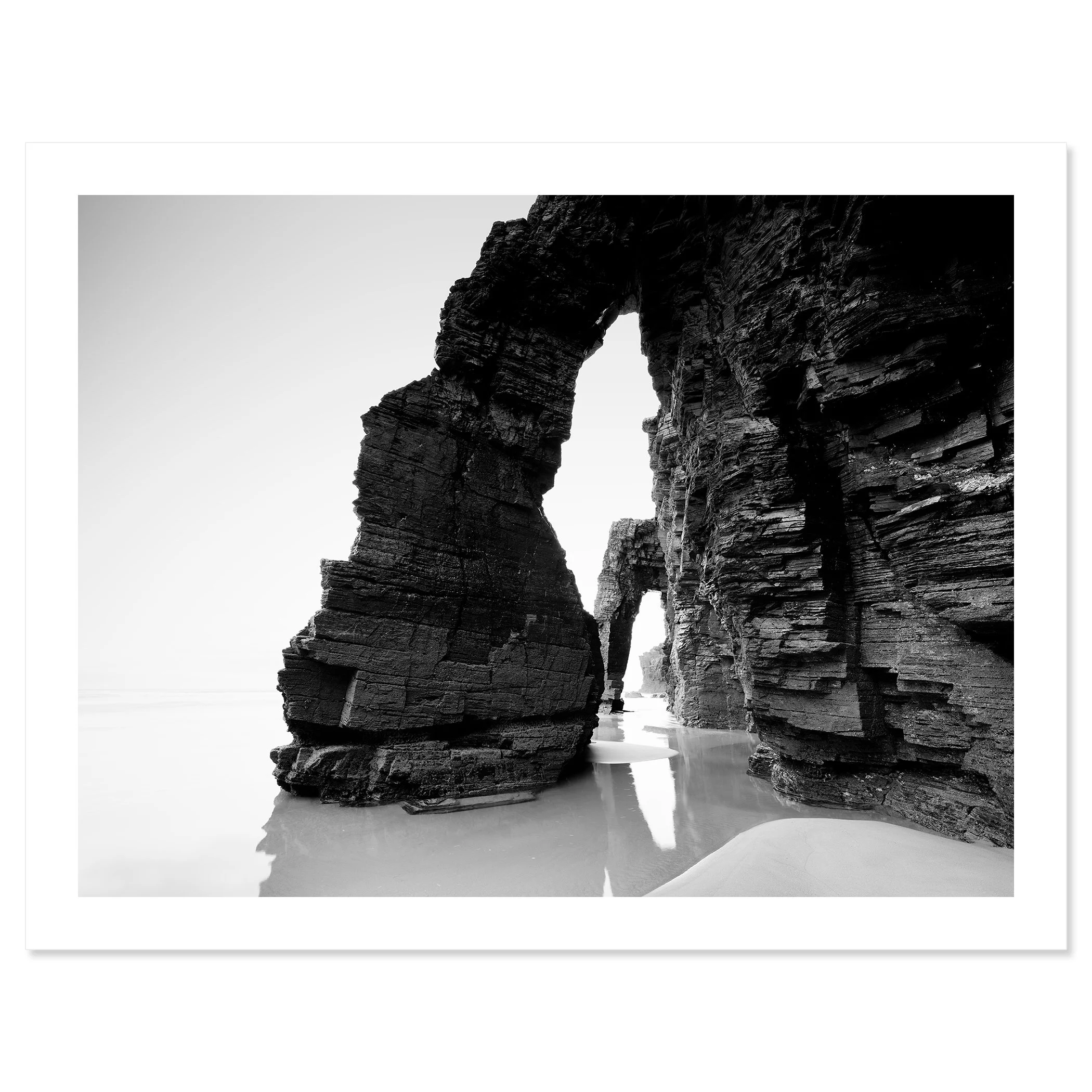 Gerald Berghammer - Black and white beach seascape photography. Large natural rock arch formations on a beach with water reflecting the rocks. Fine art print only