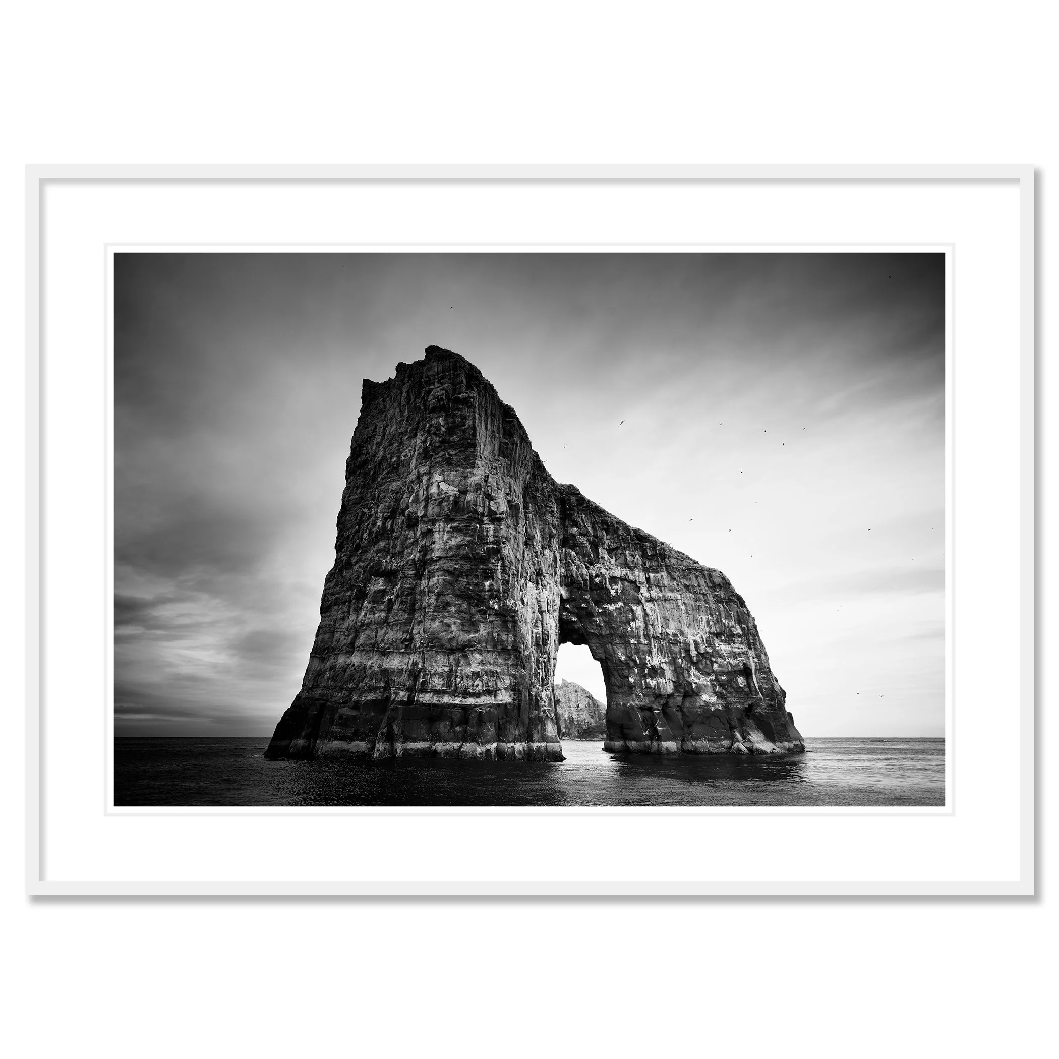 Gerald Berghammer - Black and white seascape photography.  Large natural rock formation with an arch in the middle, surrounded by water and a cloudy sky. Classic framed white