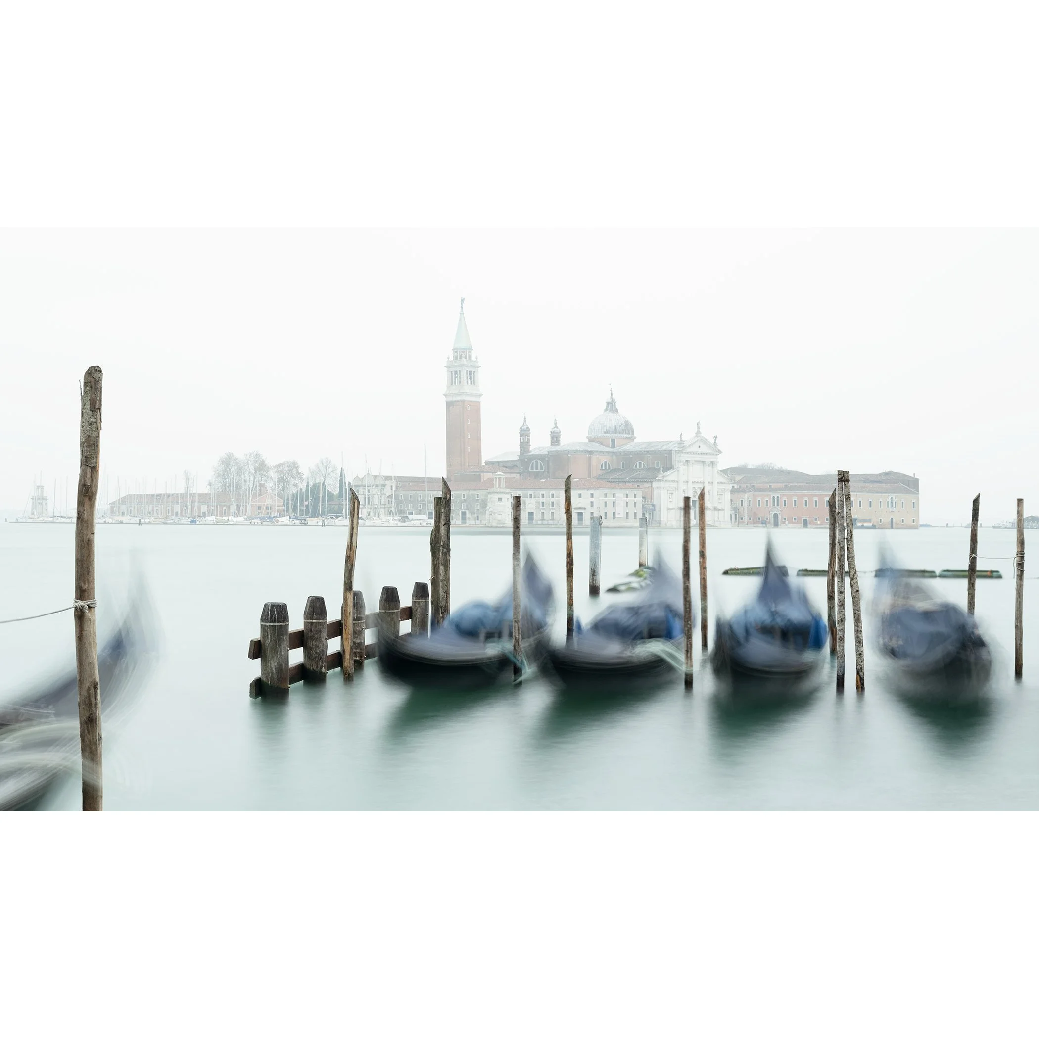 Gerald Berghammer - Color cityscape photography. Gondolas docked along wooden posts on a misty water canal and in back San Giorgio Maggiore Church.