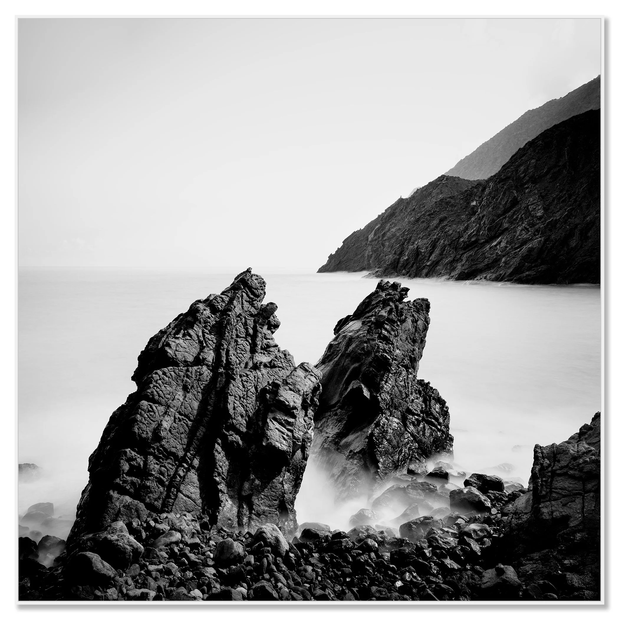 Black and white Atlantic seascape: rocky shoreline, large sea boulders, and mountains in the distance – framed ArtBox white