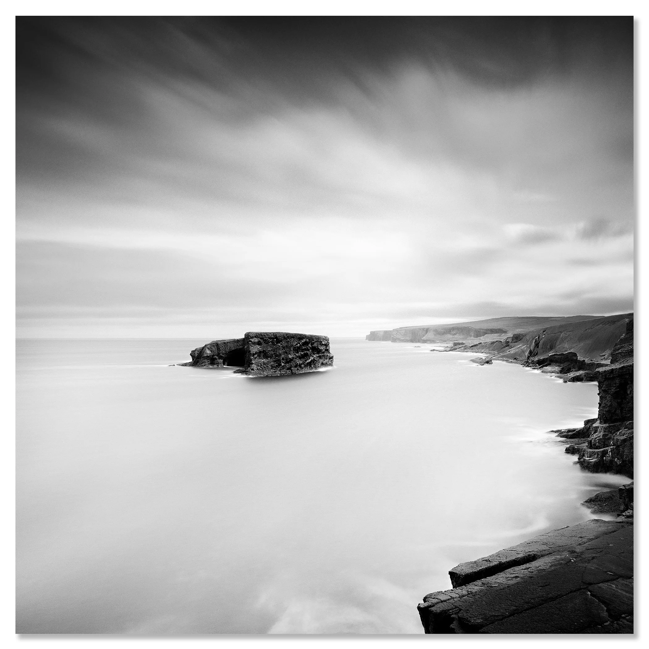 Gerald Berghammer - Black and white long exposure seascape photography. Rocky coastal landscape with cliffs and a large rock formation in the ocean. Chromaluxe frameless