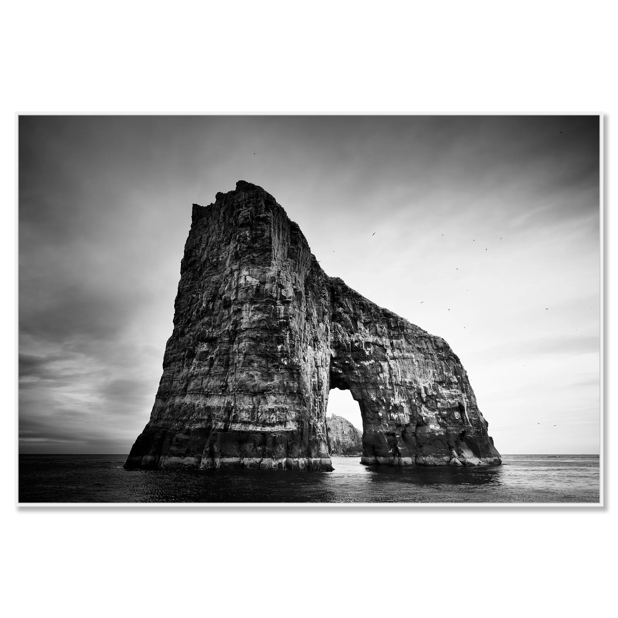 Gerald Berghammer - Black and white seascape photography.  Large natural rock formation with an arch in the middle, surrounded by water and a cloudy sky. Chromaluxe framed white