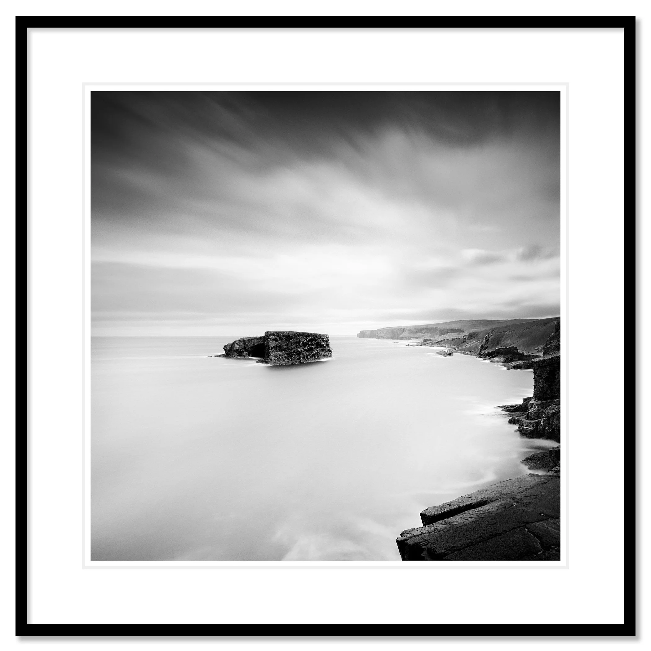 Gerald Berghammer - Black and white long exposure seascape photography. Rocky coastal landscape with cliffs and a large rock formation in the ocean. Classic framed black
