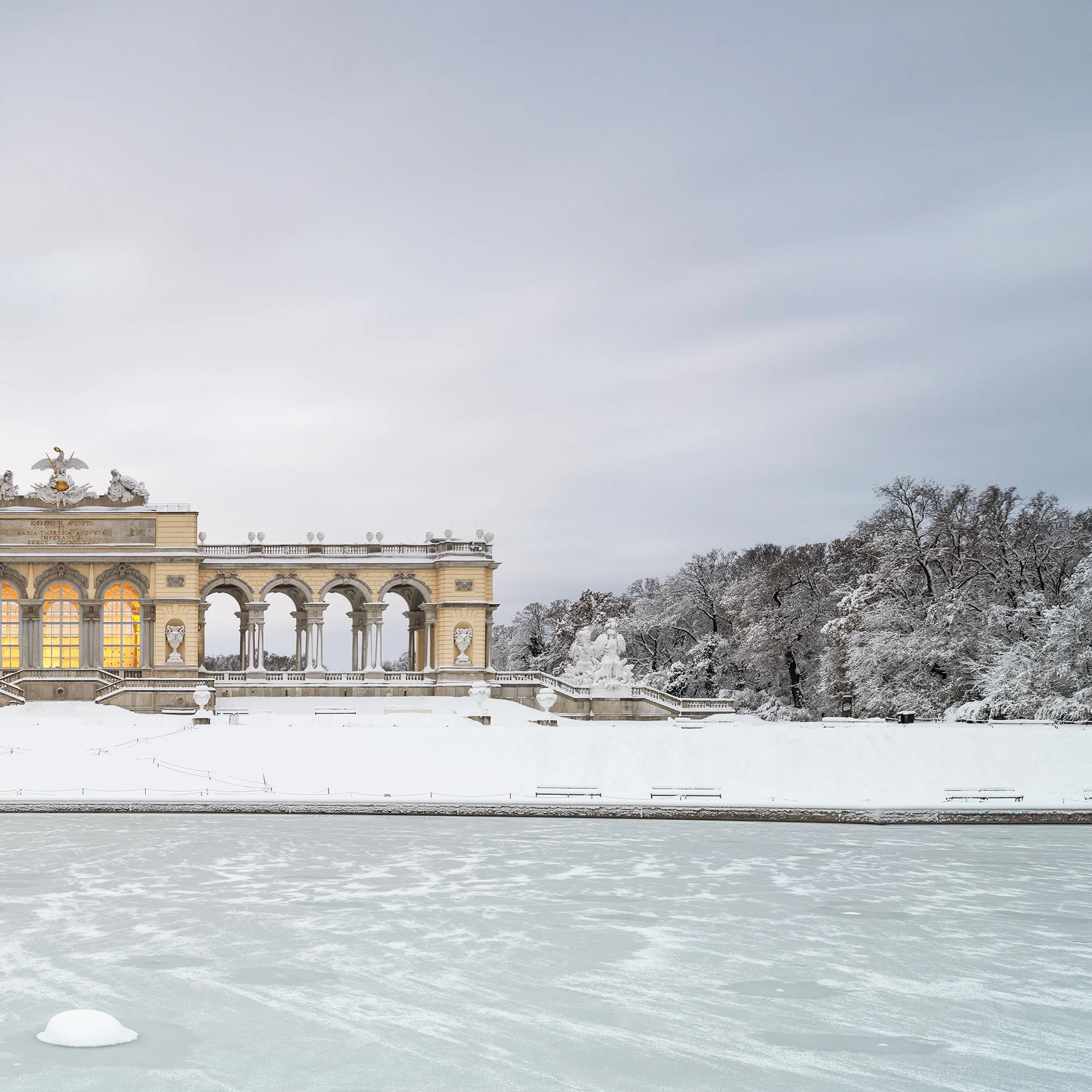Gerald Berghammer - Color Photography. A historic building on a snow-covered landscape, surrounded by leafless trees, with a frozen body of water. Print detail 2