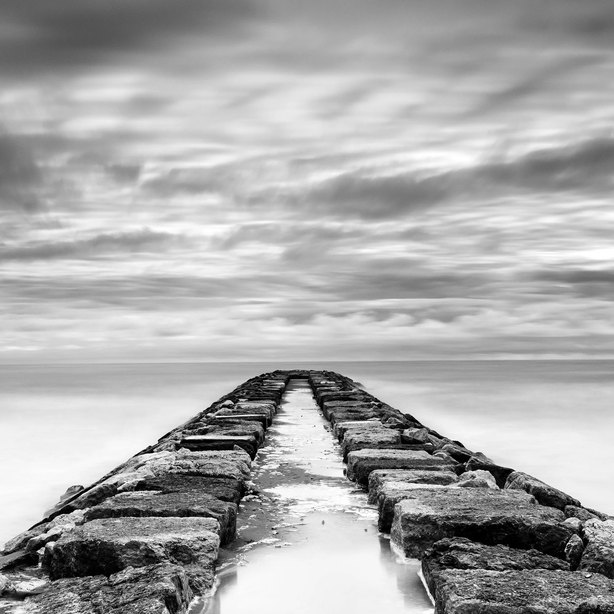 Rock Pier, Panorama Study 1 by Gerald Berghammer, close-up of the stone breakwater extending towards the horizon beneath a dramatic sky.
