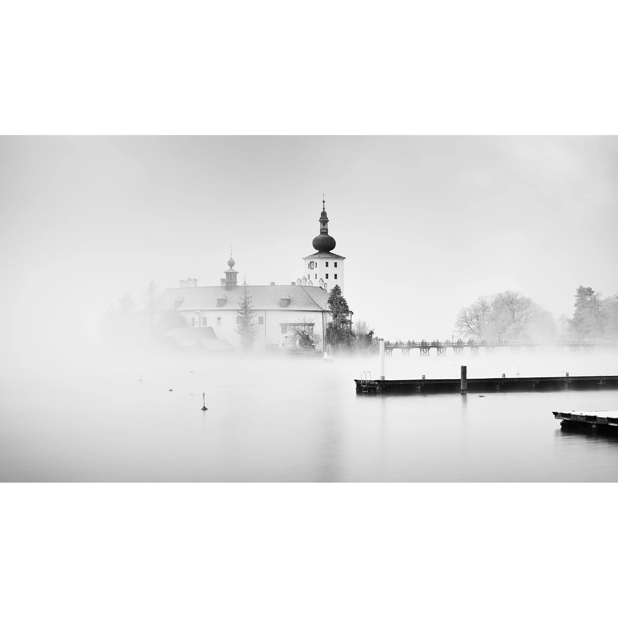 © 2022 Gerald Berghammer - Black and white cityscape photography. Schloss Ort - The historic church surrounded by mist over a lake with docks in the foreground.