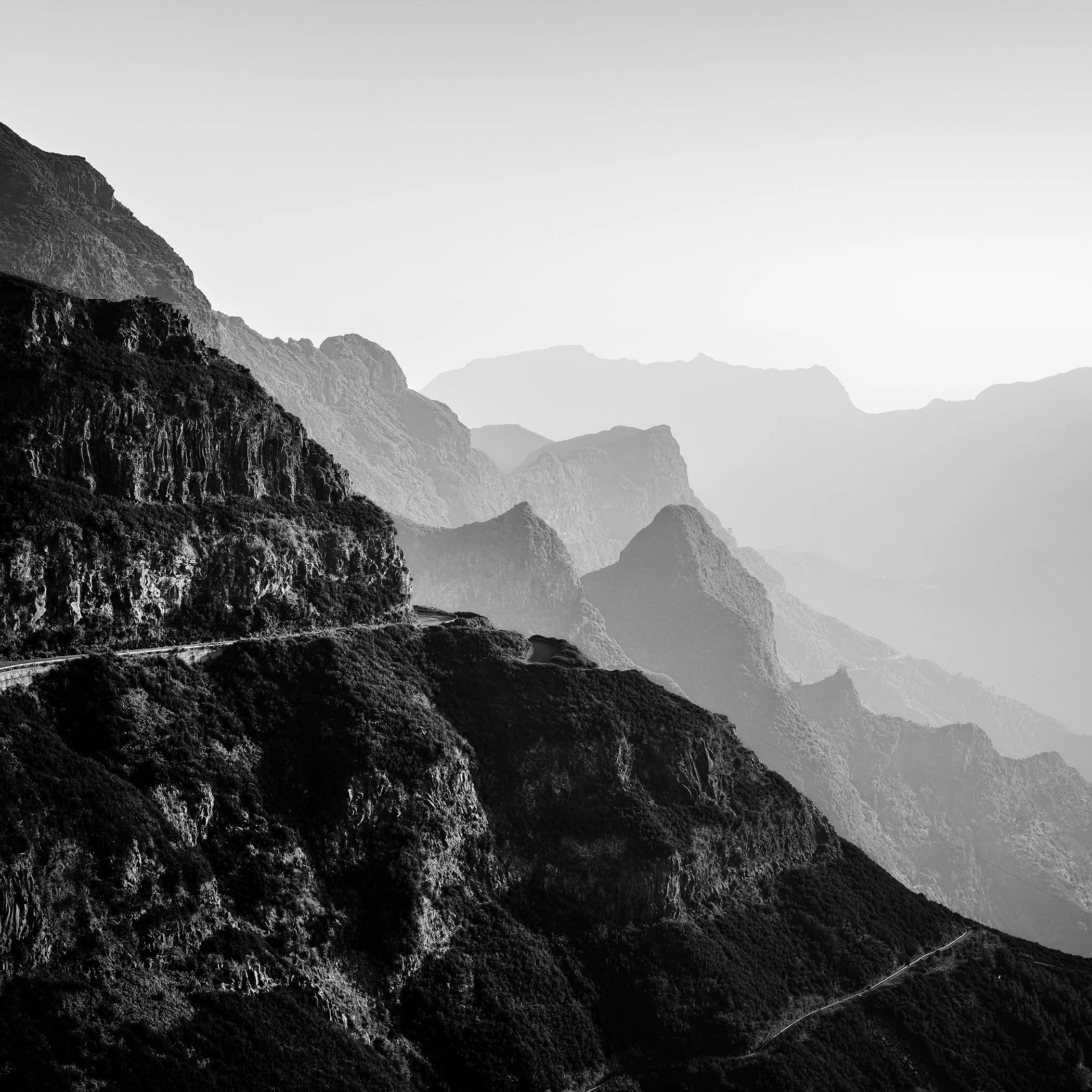 Misty black and white mountain range with steep rock faces and a serpentine road along the hillside.