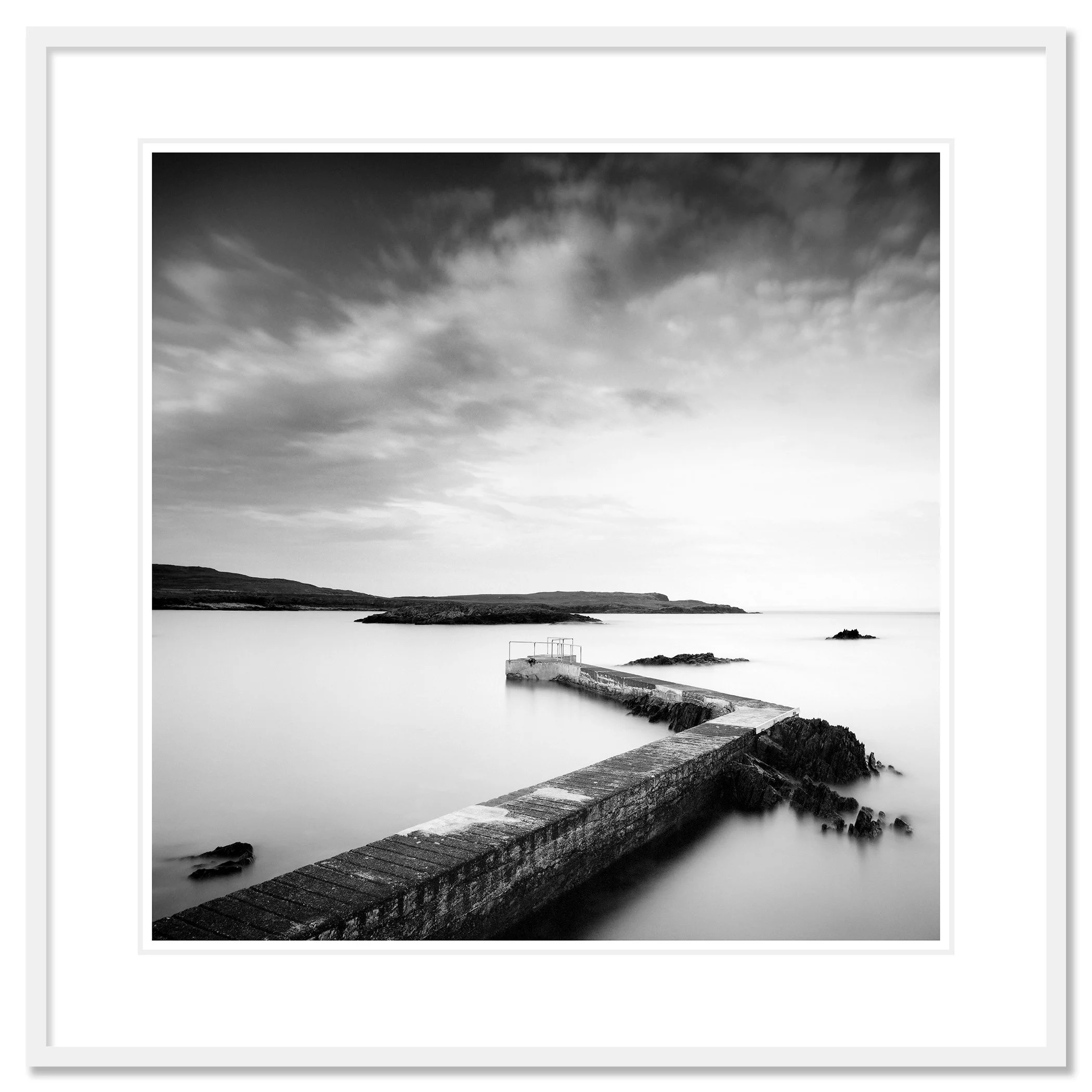 © 2014 Gerald Berghammer - Black and white seascape photography. A Concrete pier extends into calm seawater with rocky edges, under a cloudy sky. Classic framed white