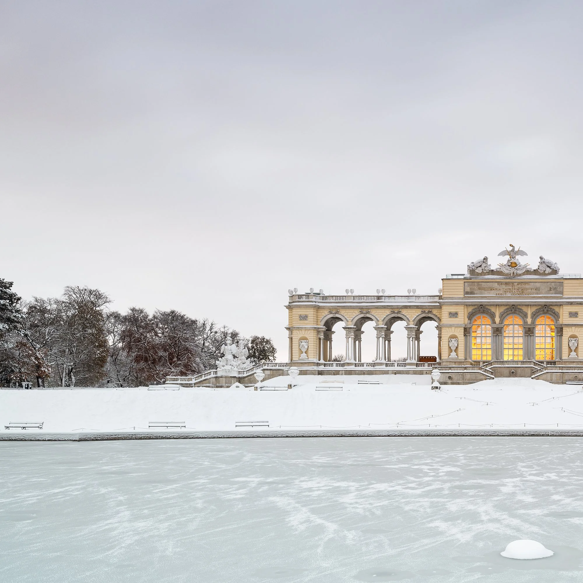 Gerald Berghammer - Color Photography. A historic building on a snow-covered landscape, surrounded by leafless trees, with a frozen body of water. Print detail 1