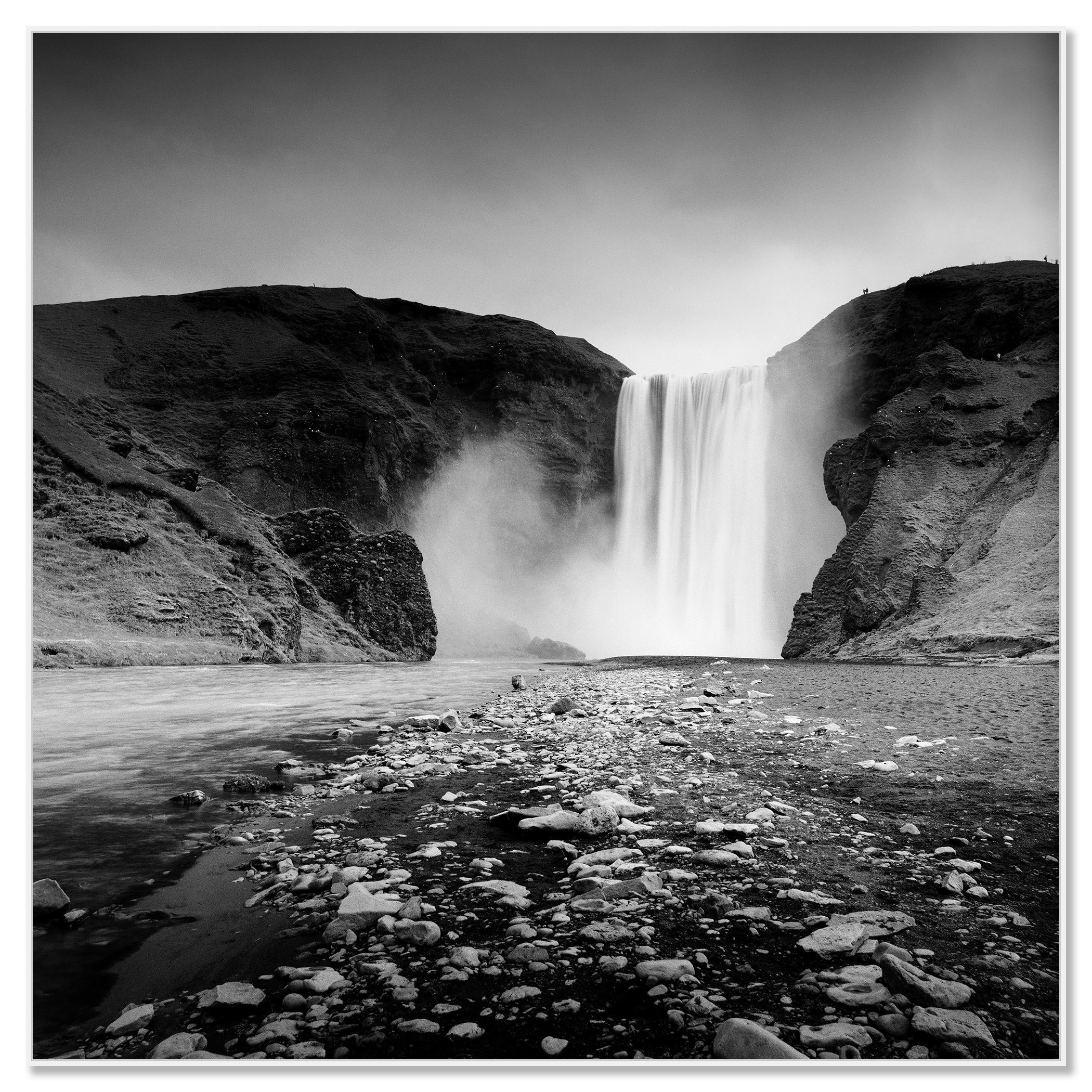 Black and white long-exposure photo of a large waterfall between rugged cliffs into a rocky river – framed Artbox white