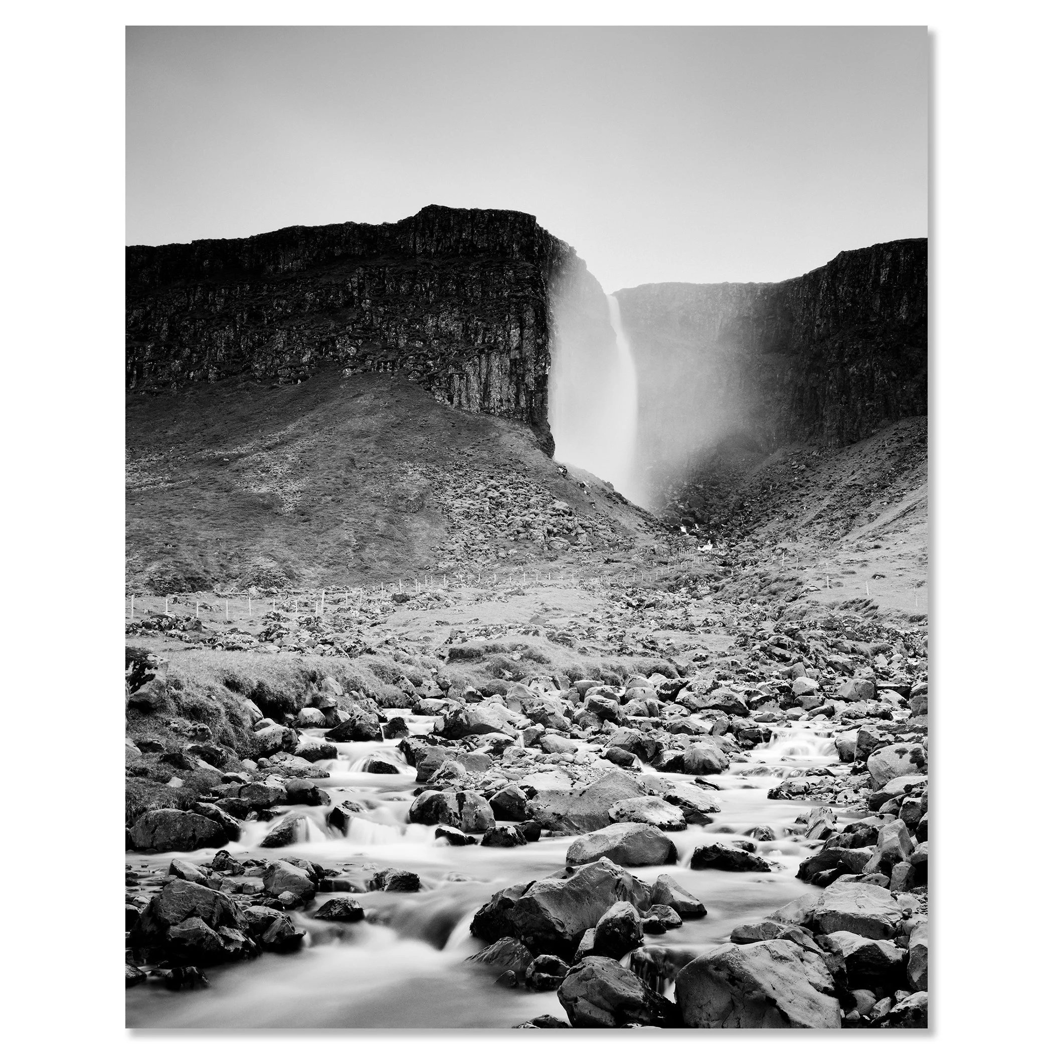 Gerald Berghammer - Black and white landscape photography. A waterfall cascading down a rocky cliff into a stream surrounded by rocks and rugged terrain. Chromaluxe frameless