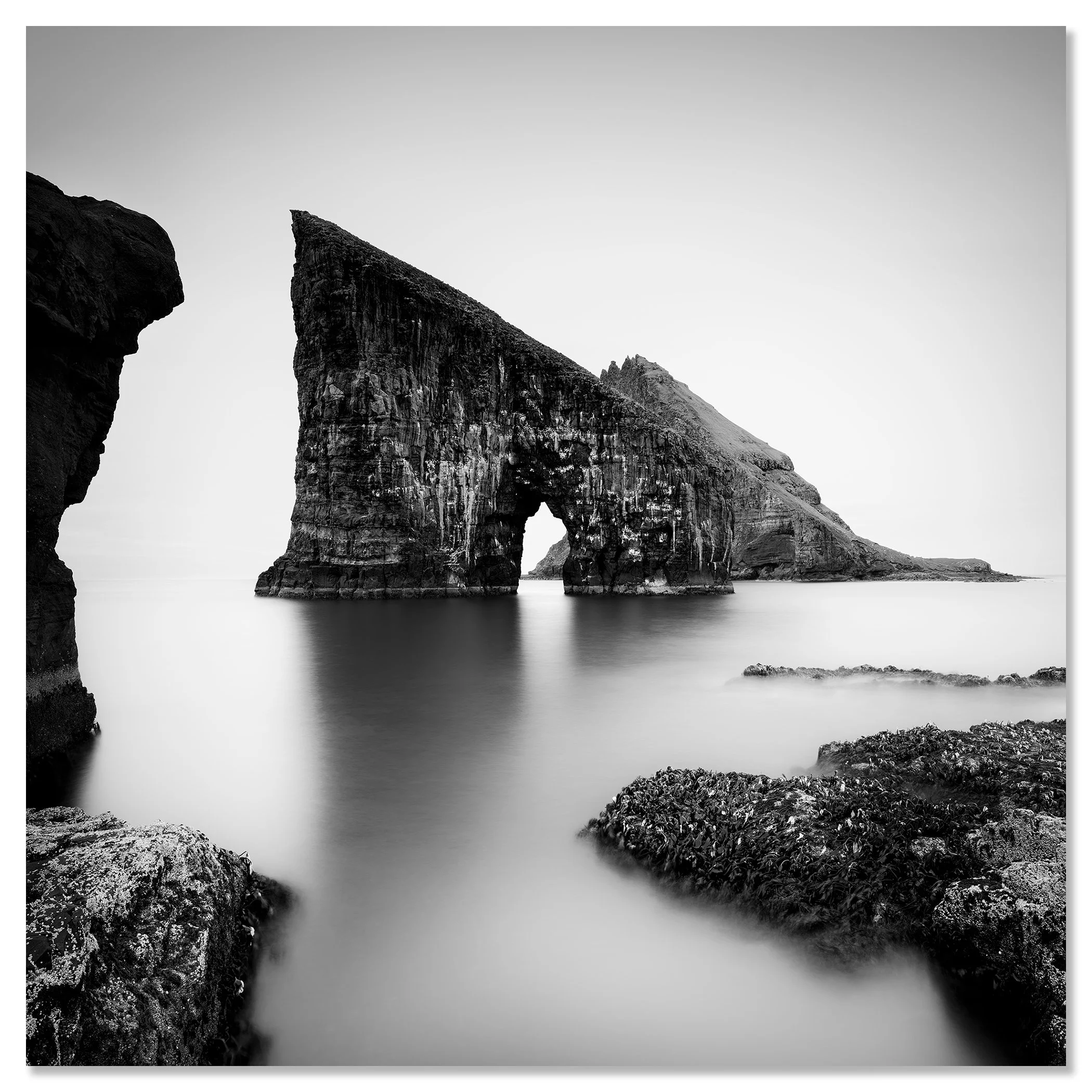 Black and white coastal landscape with a striking sea stack arch and soft long-exposure water – dibond frameless