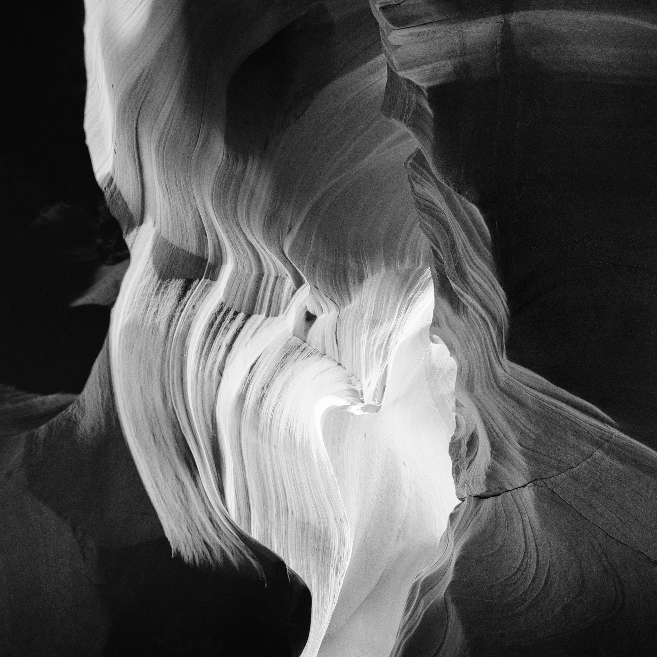 Black-and-white photograph of Antelope Canyon sandstone curves with layered textures, soft shadows and sculptural lines by Gerald Berghammer.