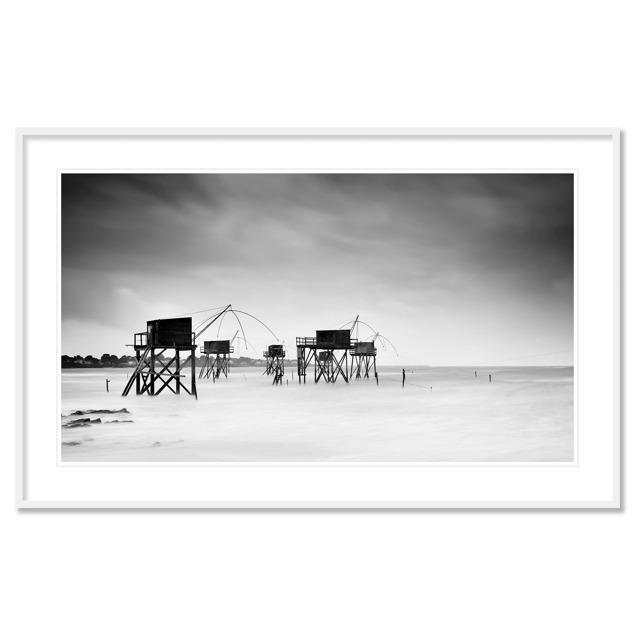 Gerald Berghammer - Black and white seascape photography. Fishing huts on stilts over water, with fishing nets hanging from the structures, under a cloudy sky. Classic framed white
