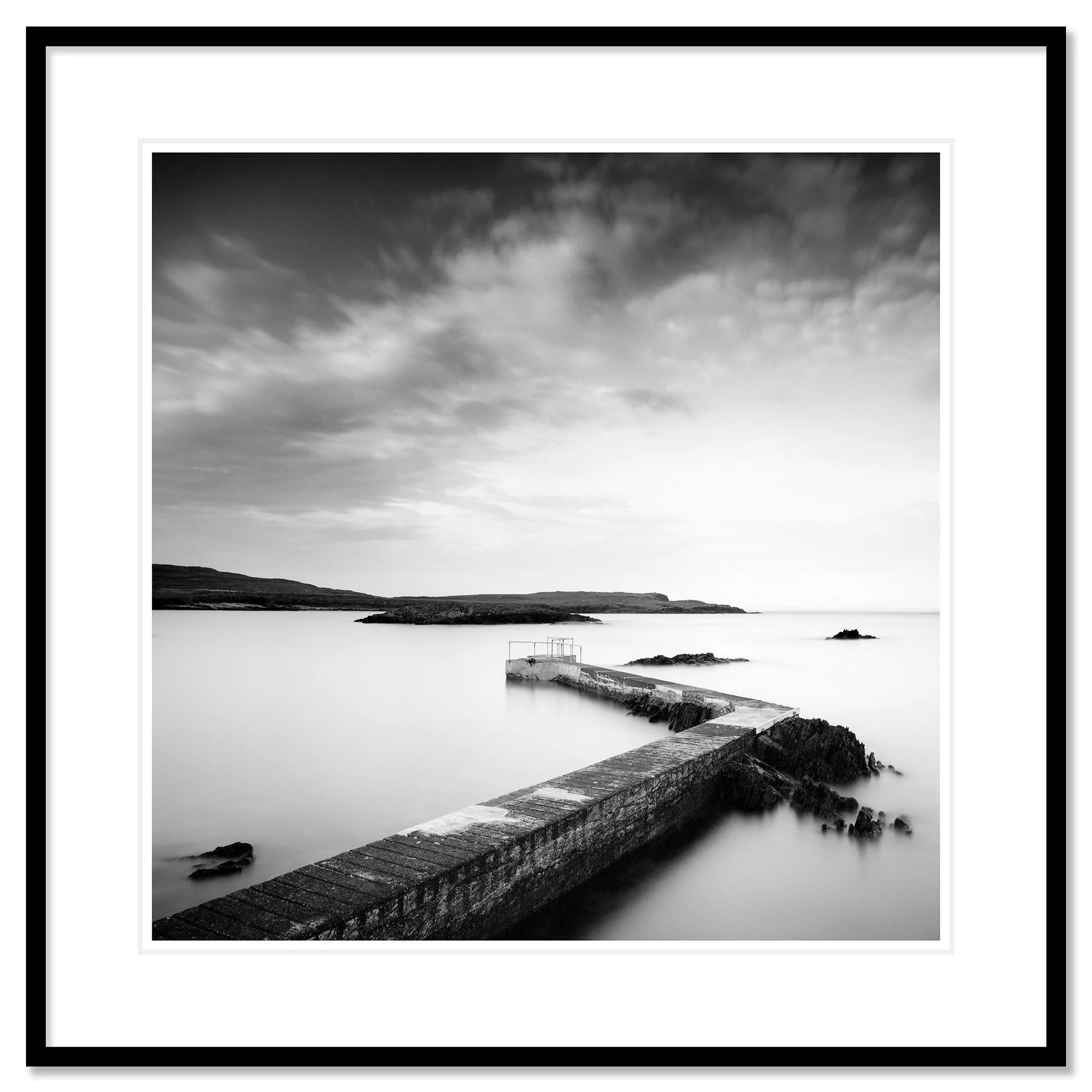 © 2014 Gerald Berghammer - Black and white seascape photography. A Concrete pier extends into calm seawater with rocky edges, under a cloudy sky. Classic framed black