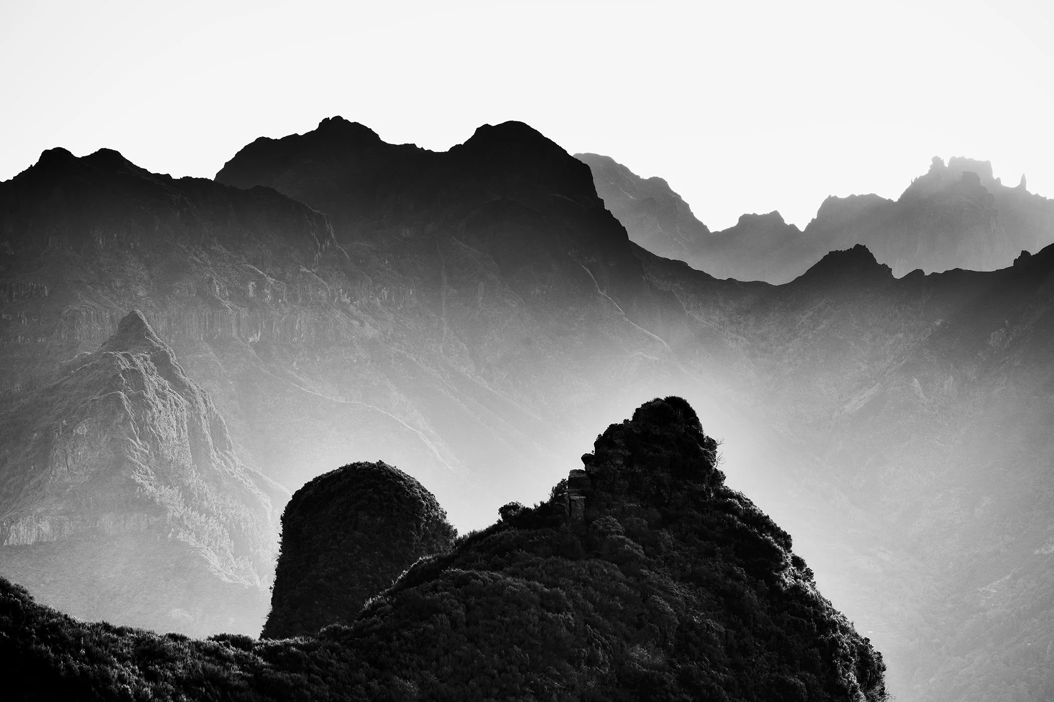 Monochrome view of dramatic mountain ridges with haze drifting through a rugged valley