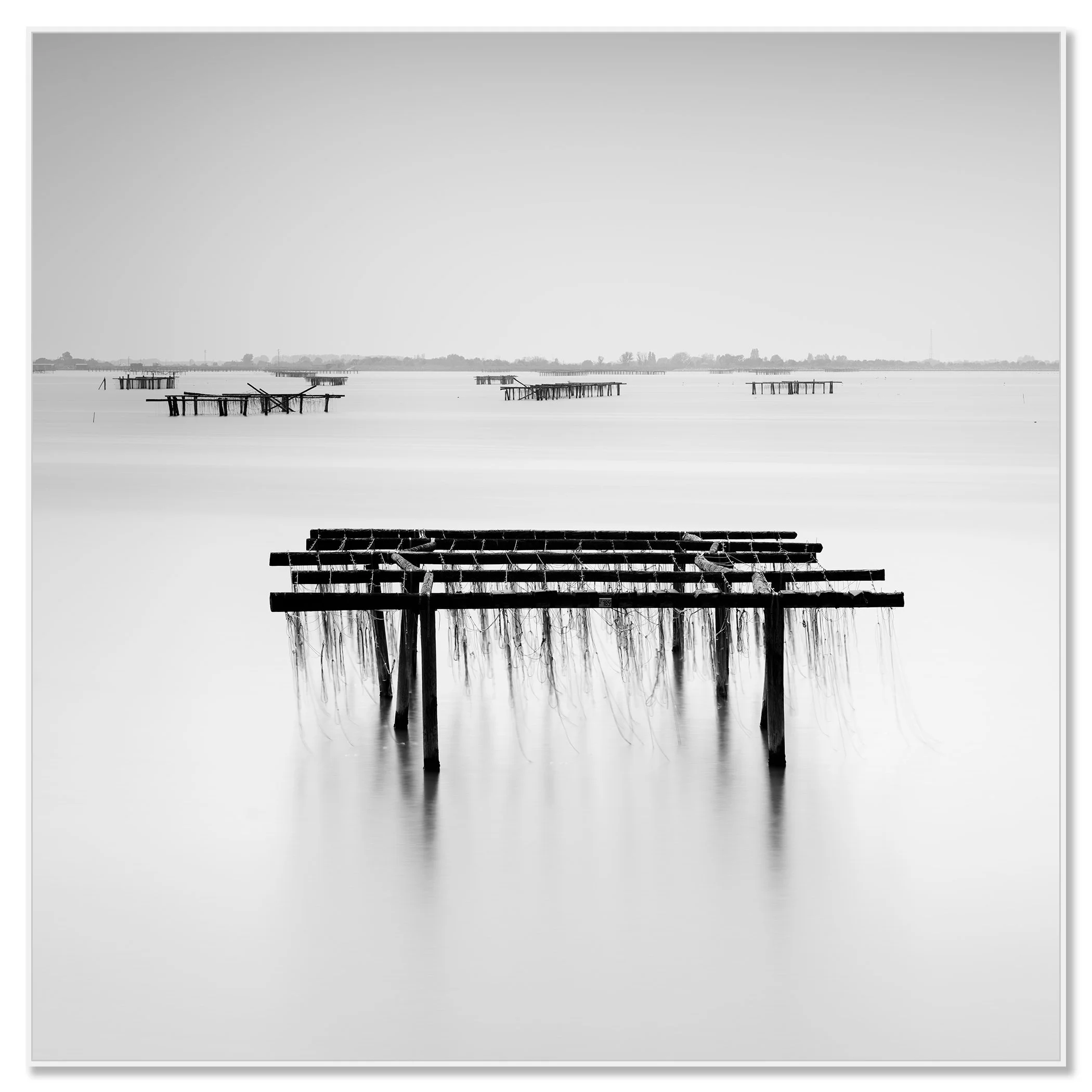 Minimalist monochrome seascape showing a wooden rack in still water with distant platforms along the horizon – framed ArtBox white
