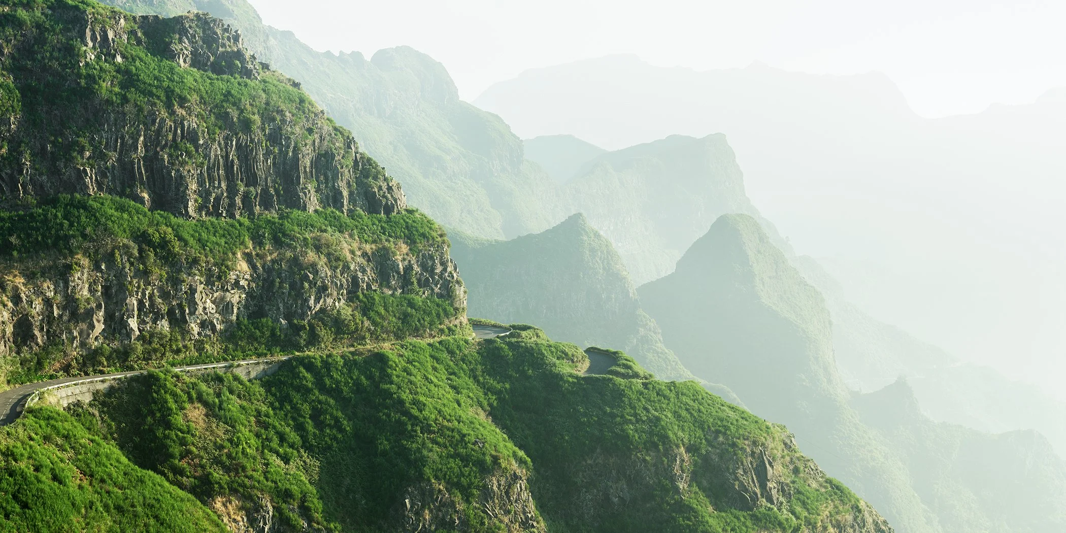 Dramatic Madeira mountain landscape with steep green volcanic cliffs, misty valleys and morning light