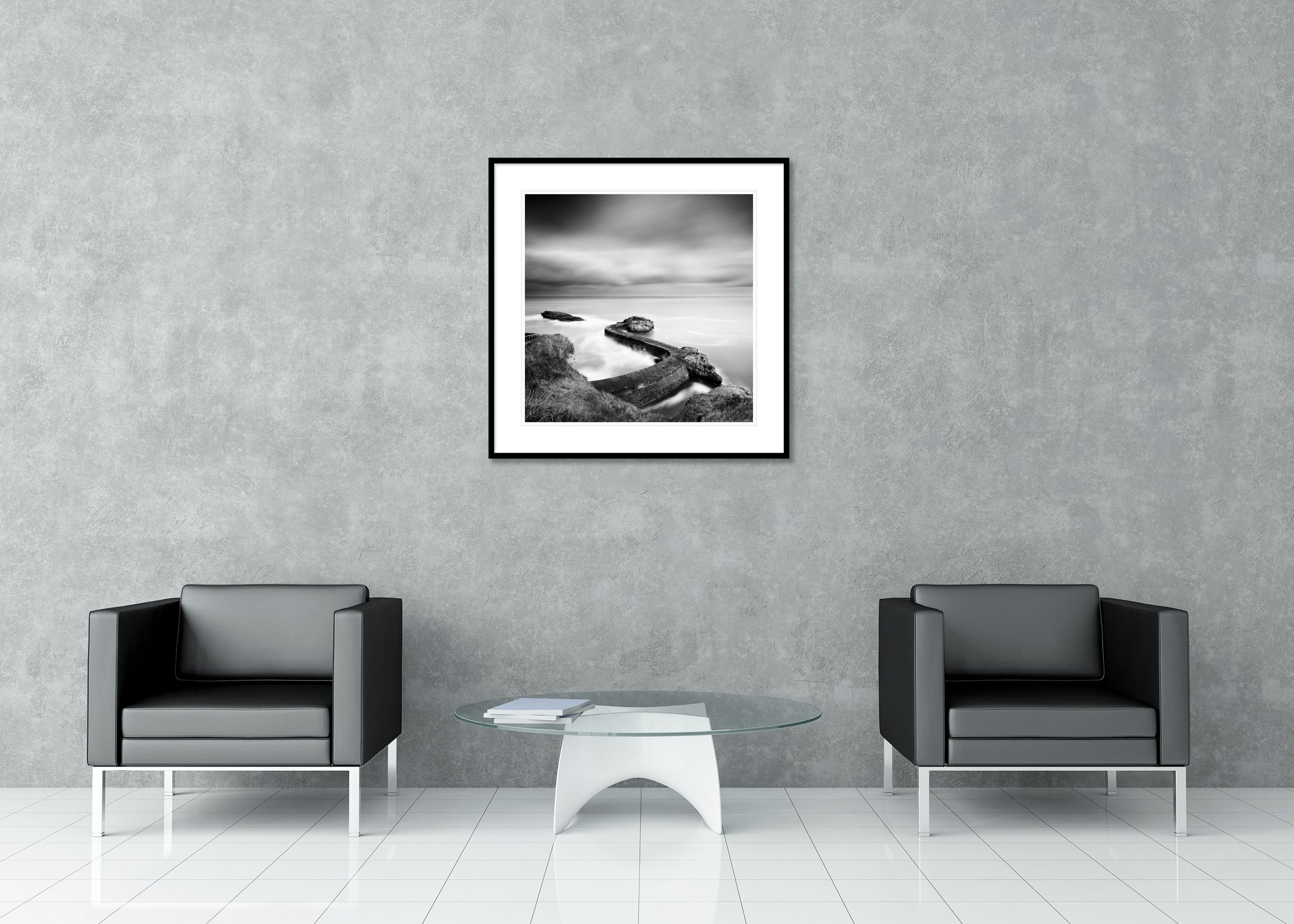Black and white print of a curved harbour breakwater pier with rocks and smooth long-exposure water, archival pigment print in a classic frame with mount.