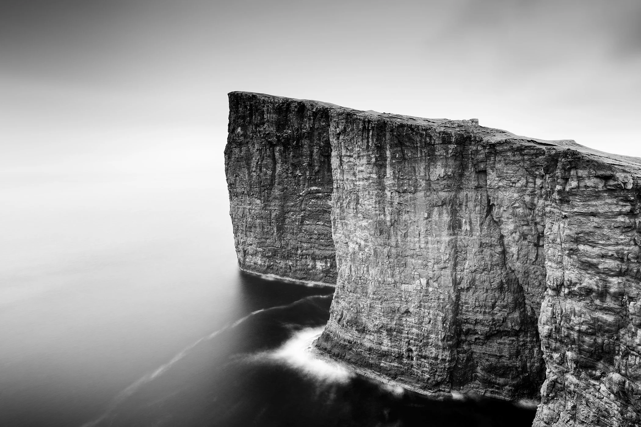 Black and white view of dramatic sea cliffs in the Faroe Islands above calm coastal waters