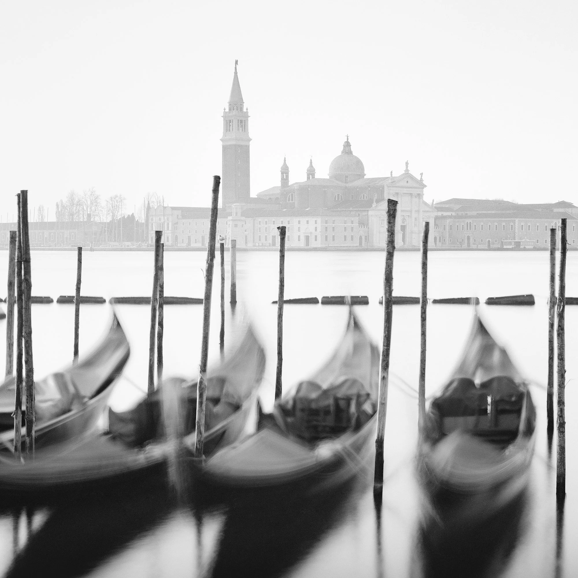 Detail of Twelve Gondolas by Gerald Berghammer showing the Basilica di San Giorgio Maggiore above blurred gondolas and wooden mooring posts.