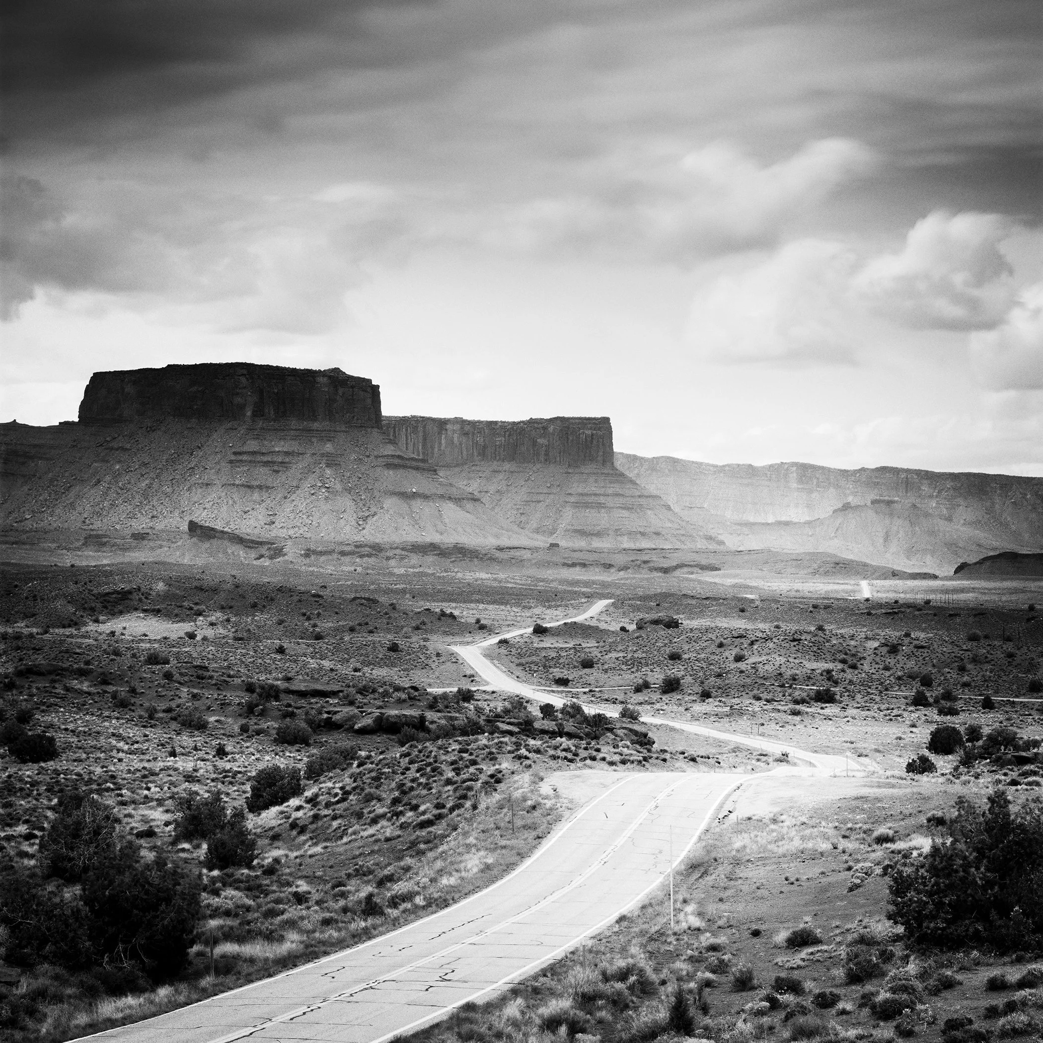 Winding road crossing a dramatic desert landscape beneath storm clouds in Utah, USA. Photo by Gerald Berghammer.