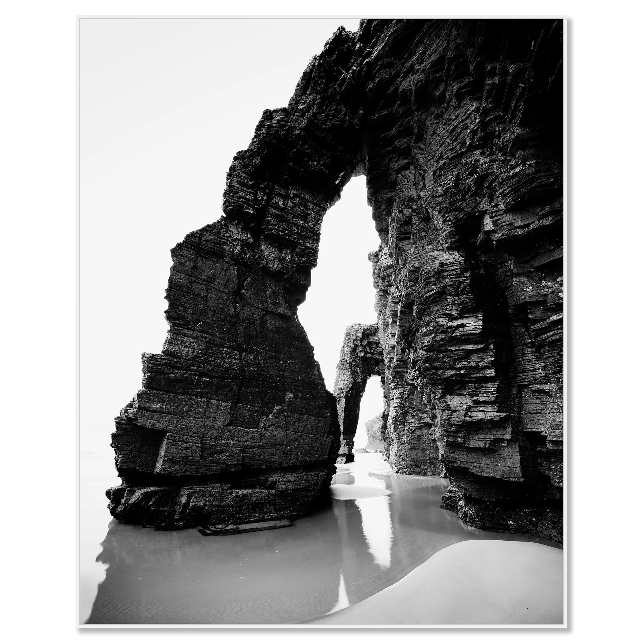 Black and white long-exposure minimalist seascape of rock arches on a beach with wet sand reflections – framed ArtBox white
