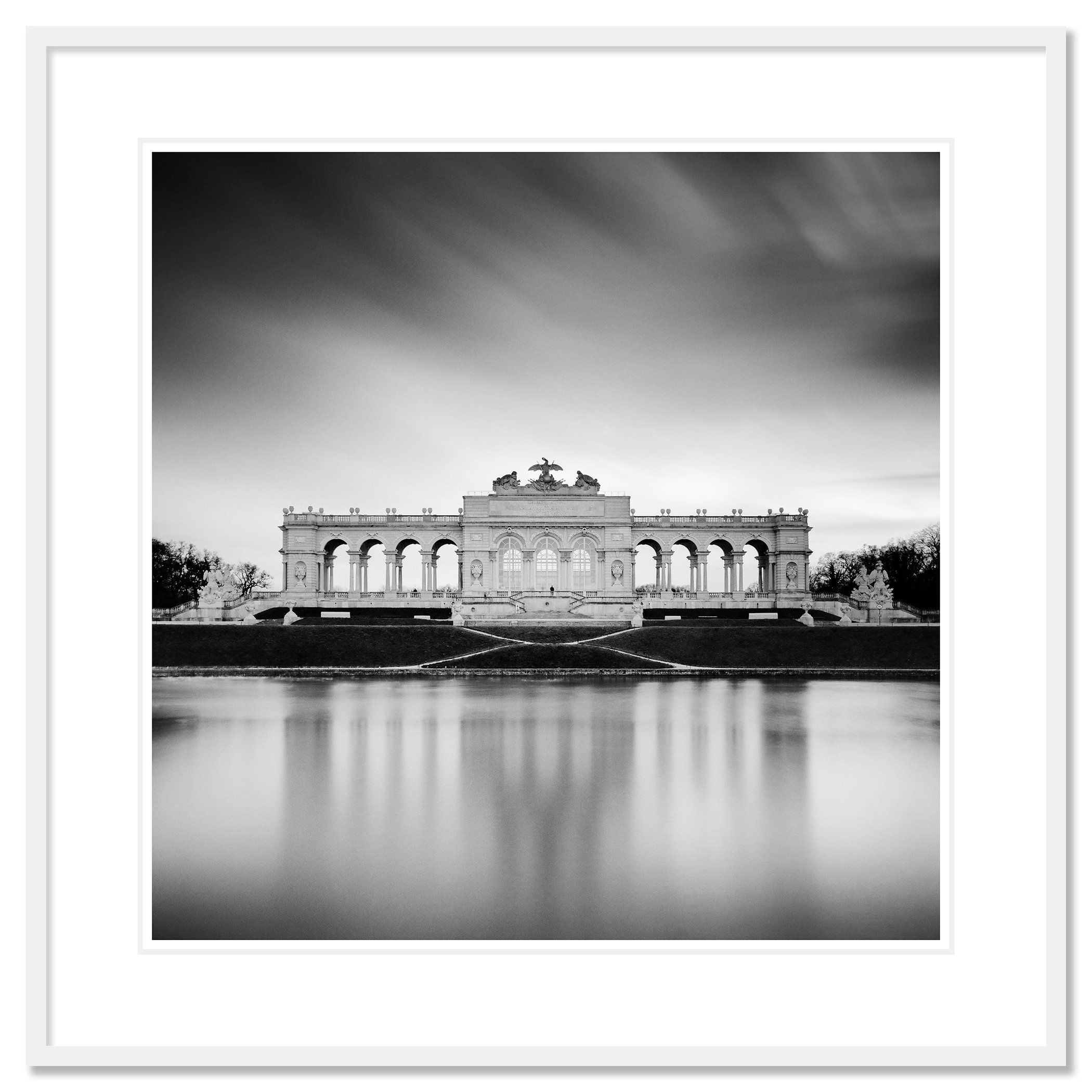 Gerald Berghammer - B&W Cityscape Photography. A large, ornate building with arches and decorative sculptures on top, reflected in a calm body of water. Classic framed white