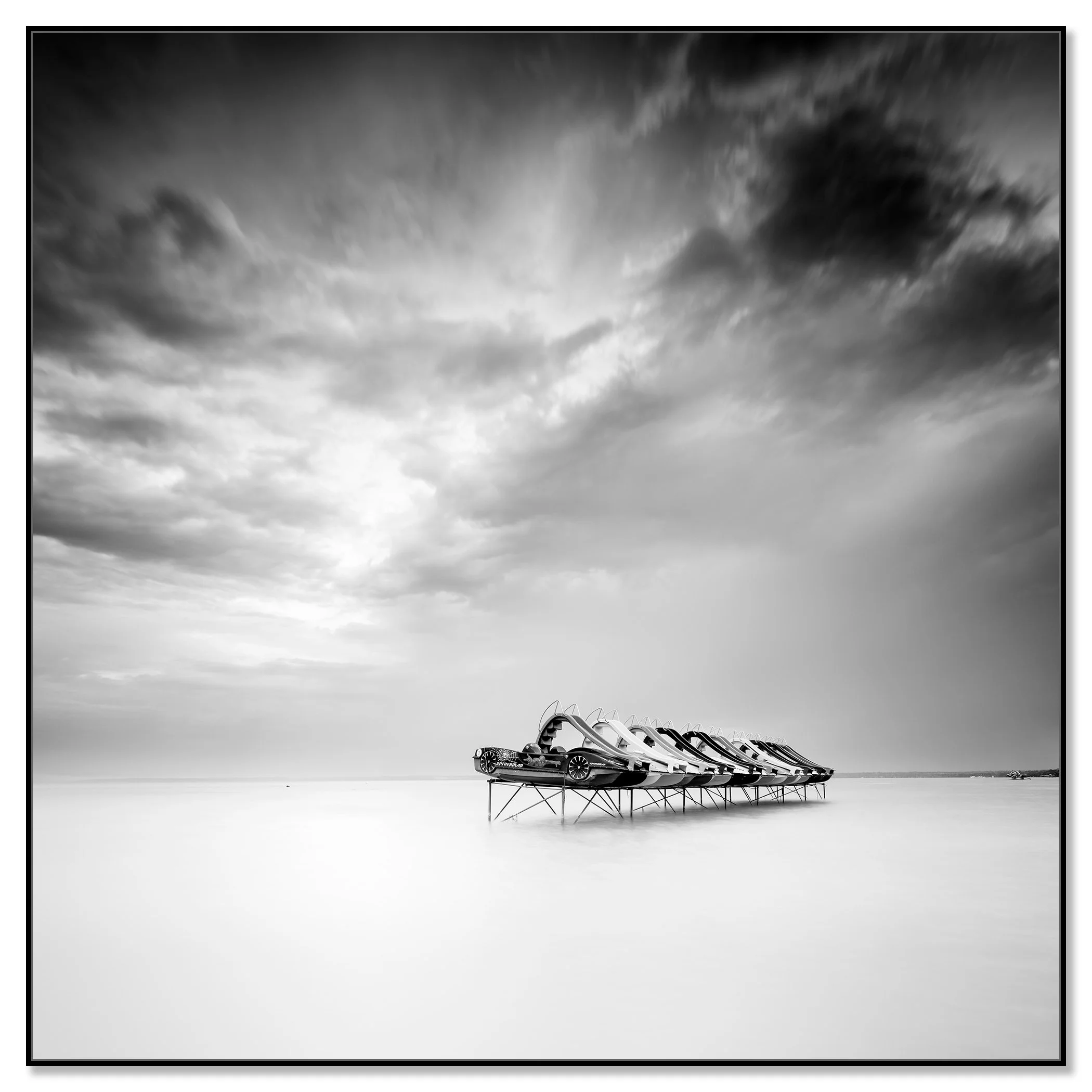 nd white long-exposure lake scene with pedal boats on stilts and a dramatic cloudy sky – framed ArtBox black