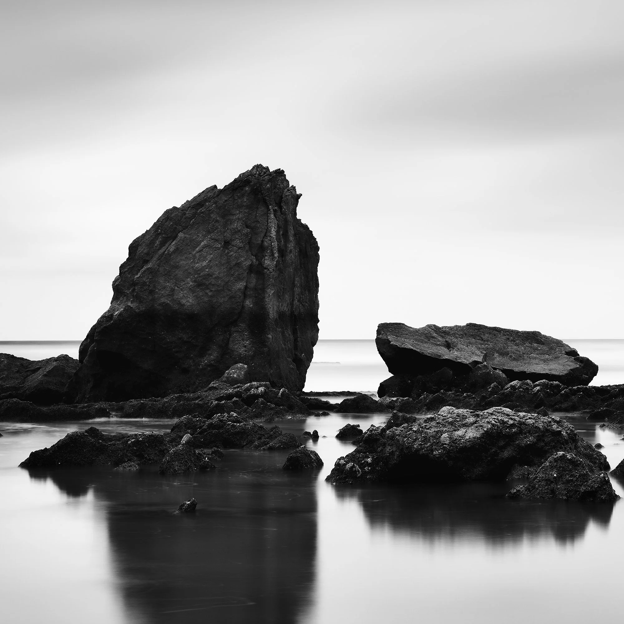 © 2023 Gerald Berghammer - Black and white minimalist beach seascape. A rocky shoreline with a large prominent rock formation in the water. Print detail 3