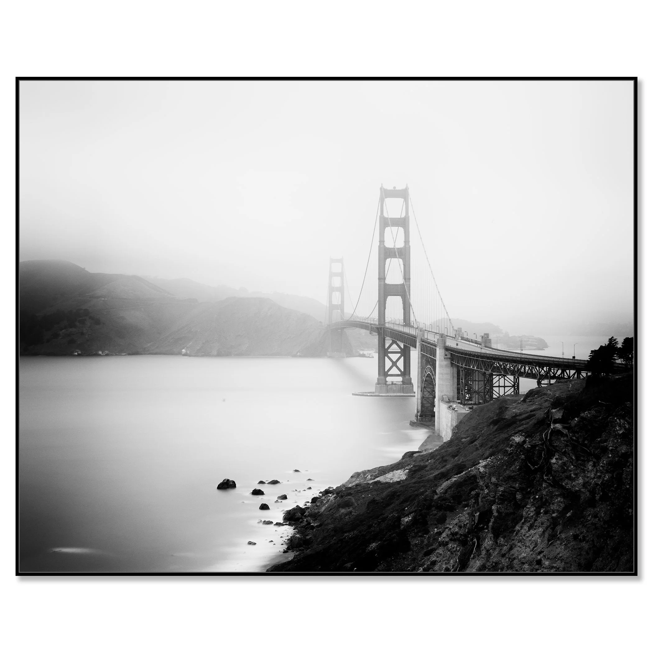 Gerald Berghammer - Black and white cityscape photography. Golden Gate Bridge in San Francisco, partially obscured by fog, viewed from a rocky shoreline. Chromaluxe framled black