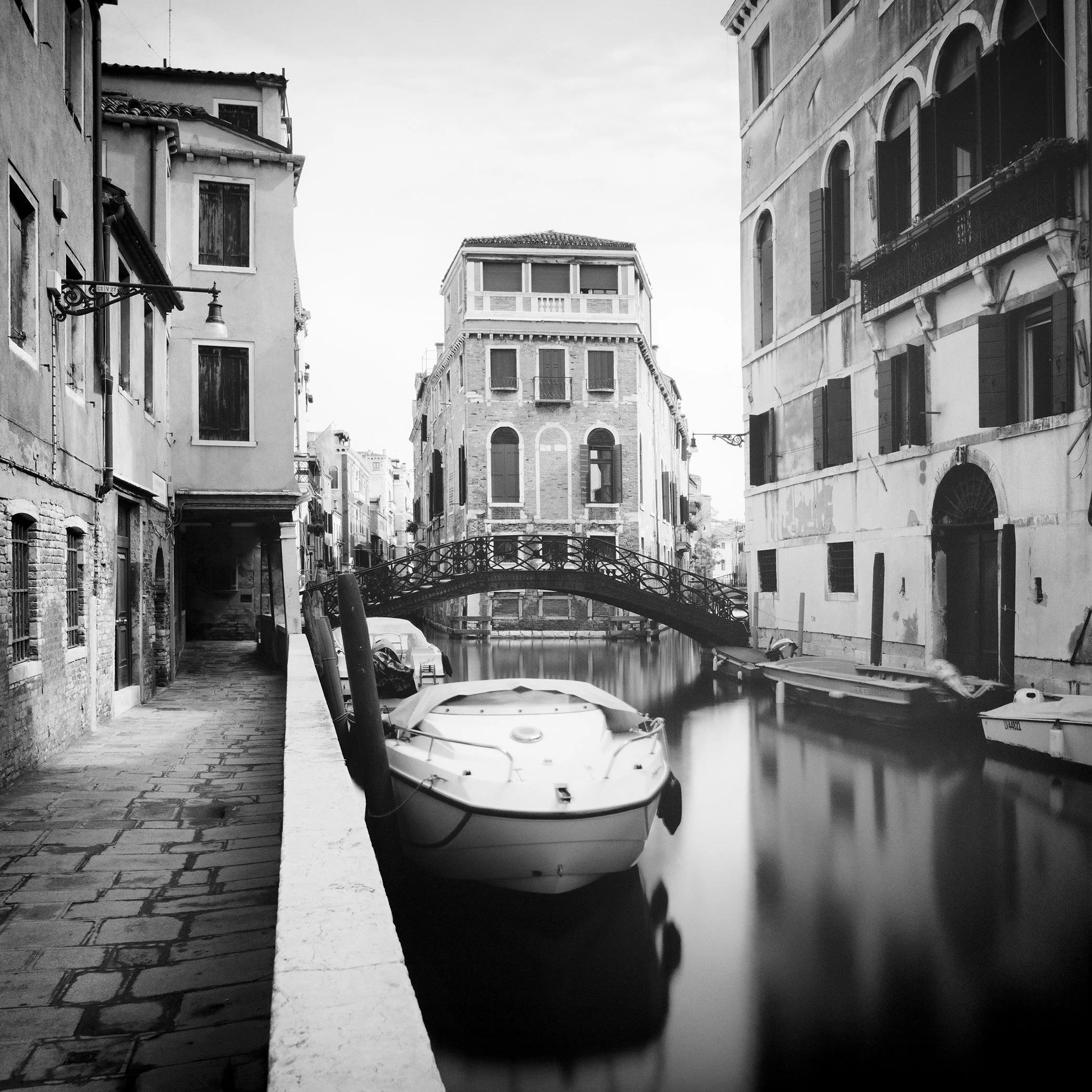 Venice canal in black and white with moored boat, arched wrought-iron bridge and historic architecture, photograph by Gerald Berghammer