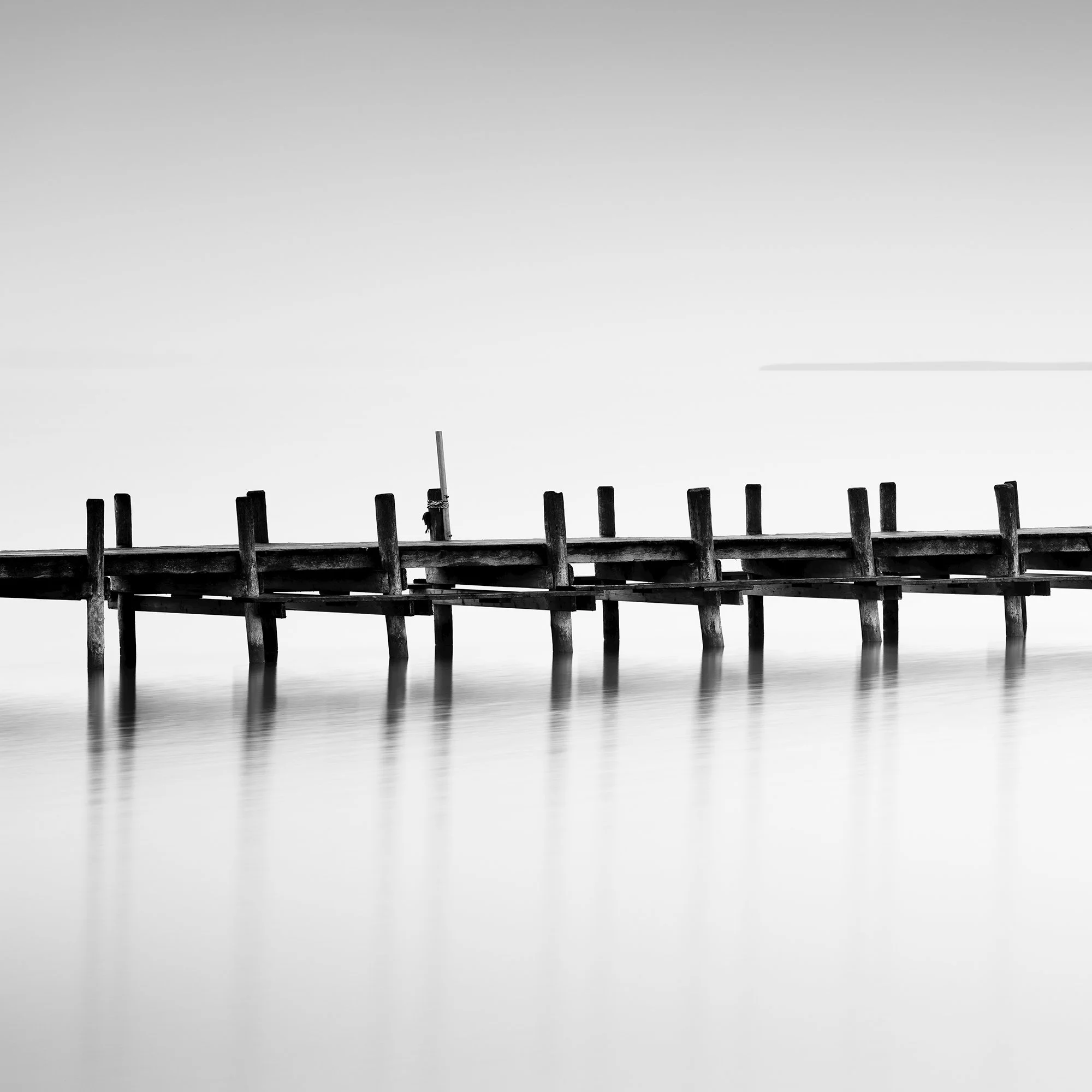 © 2023 Gerald Berghammer - Black and white long exposure waterscape photo. Wooden pier extending into calm water, with a minimalistic and serene background. Print detail 1