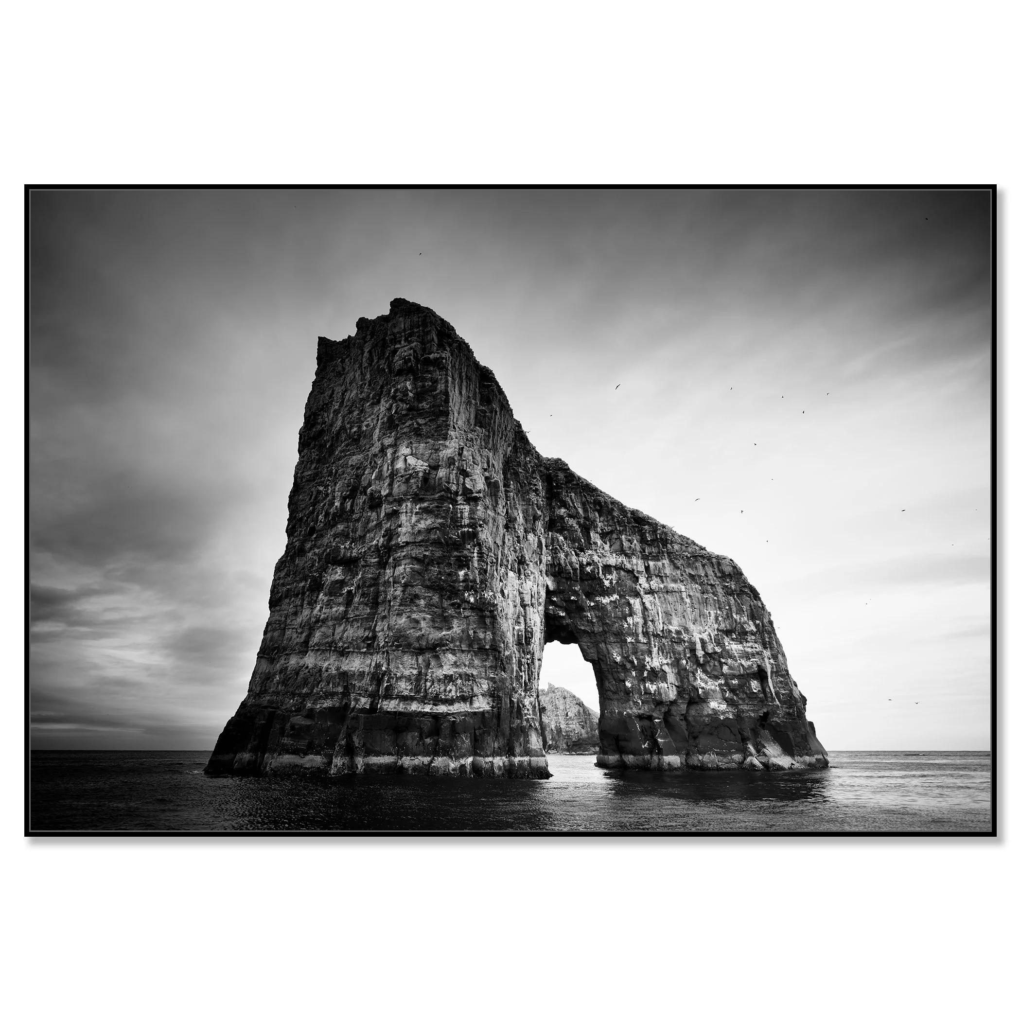 Gerald Berghammer - Black and white seascape photography.  Large natural rock formation with an arch in the middle, surrounded by water and a cloudy sky. Chromaluxe framed black