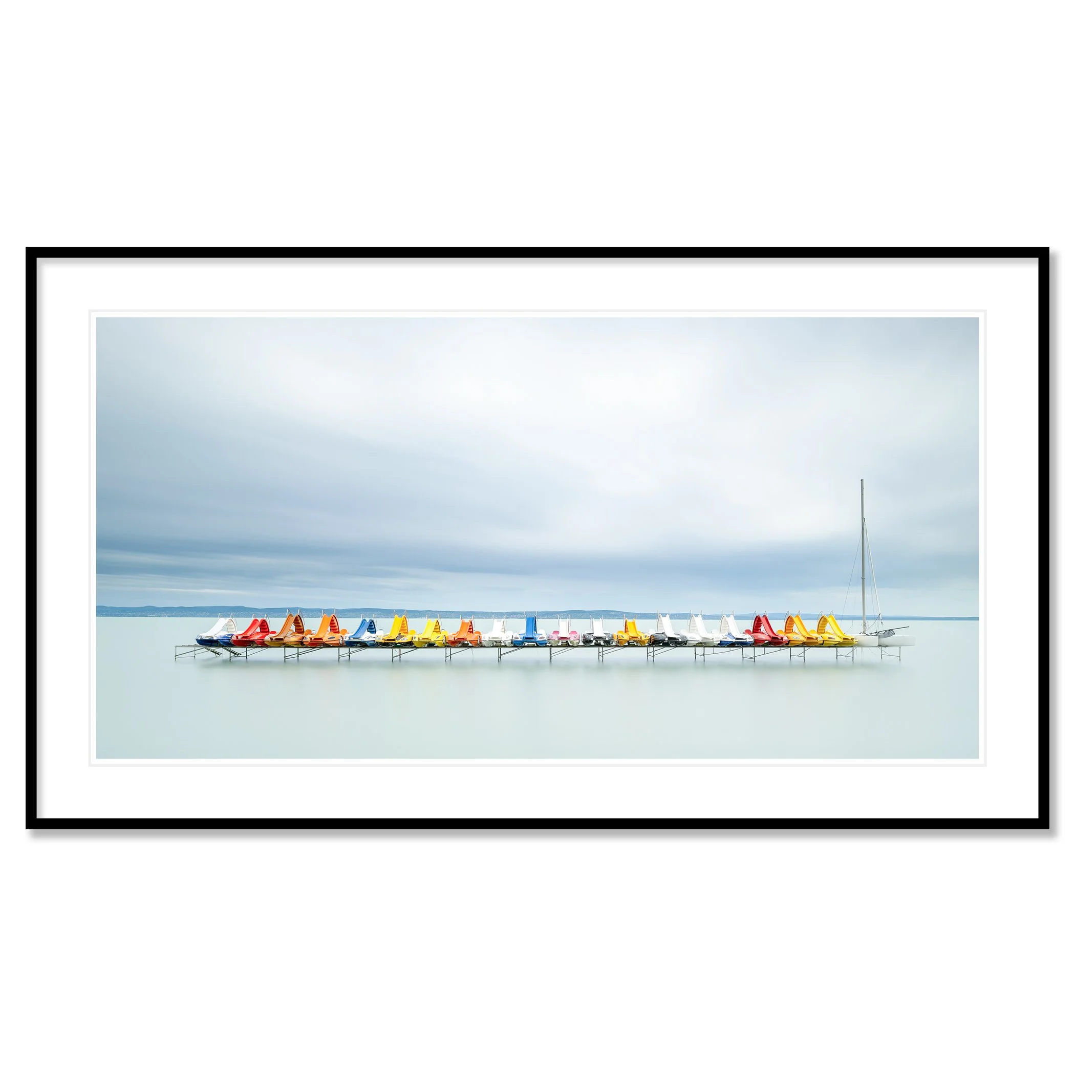 Gerald Berghammer - Color waterscape photography. Colorful pedal boats and a catamaran lined up on a dock on a calm body of water under a cloudy sky. Classic framed black
