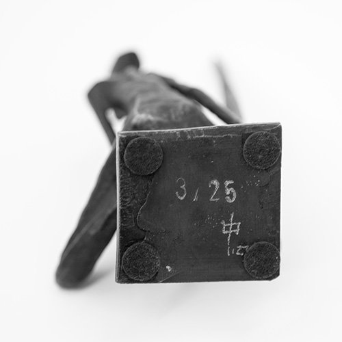 It shows the underside of a bronze sculpture, photographed from a very low angle with shallow depth of field.