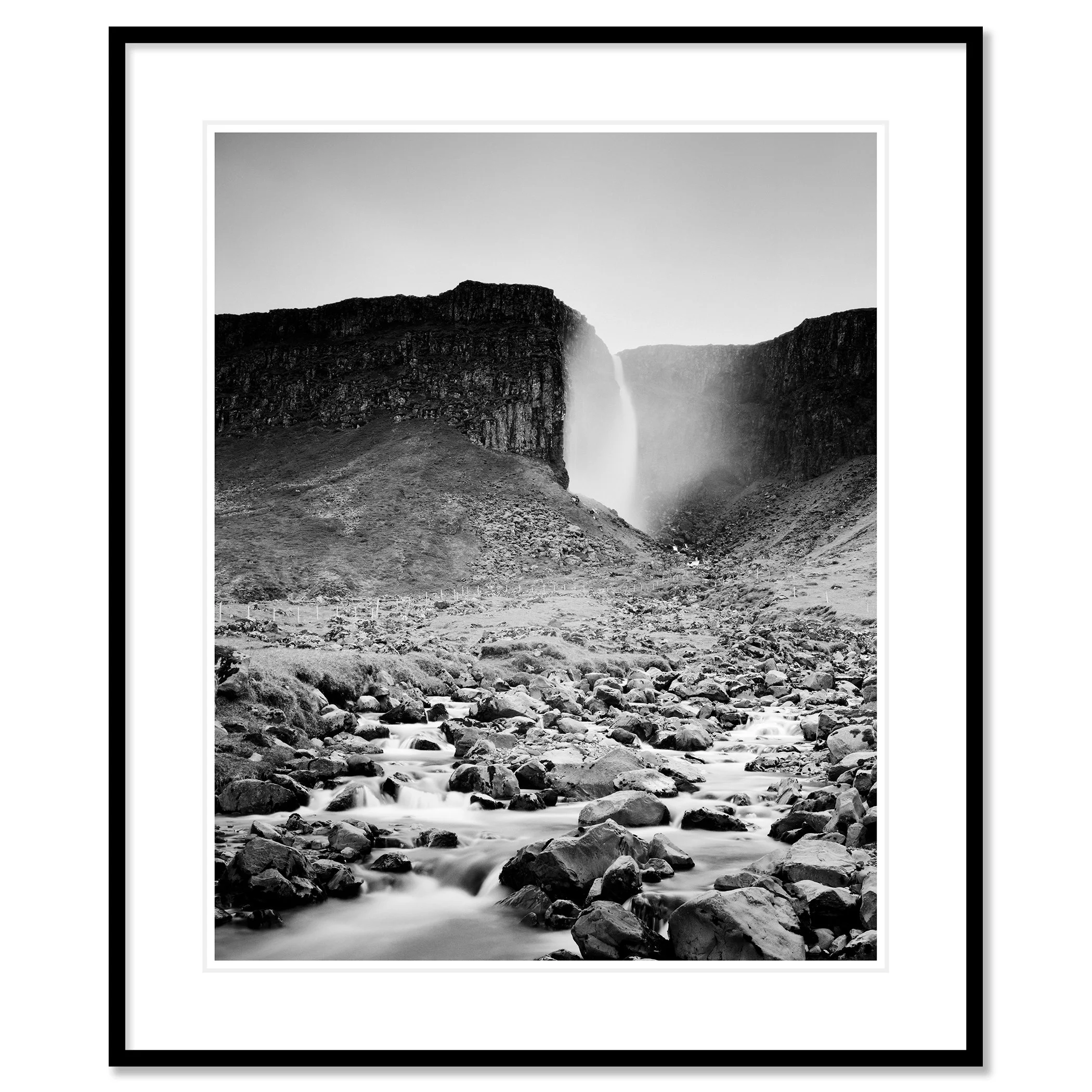 Gerald Berghammer - Black and white landscape photography. A waterfall cascading down a rocky cliff into a stream surrounded by rocks and rugged terrain. Classic framed black
