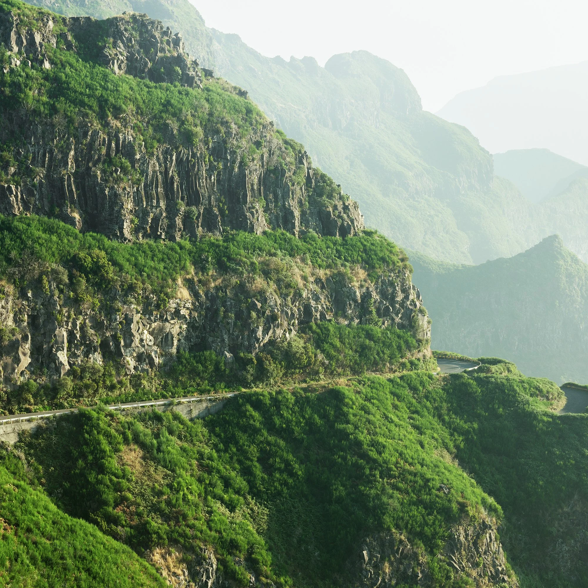 © 2021 Gerald Berghammer - Color Fine Art Landscape Photography. A winding mountain road through lush green cliffs and misty mountains in the background. Print detail 1