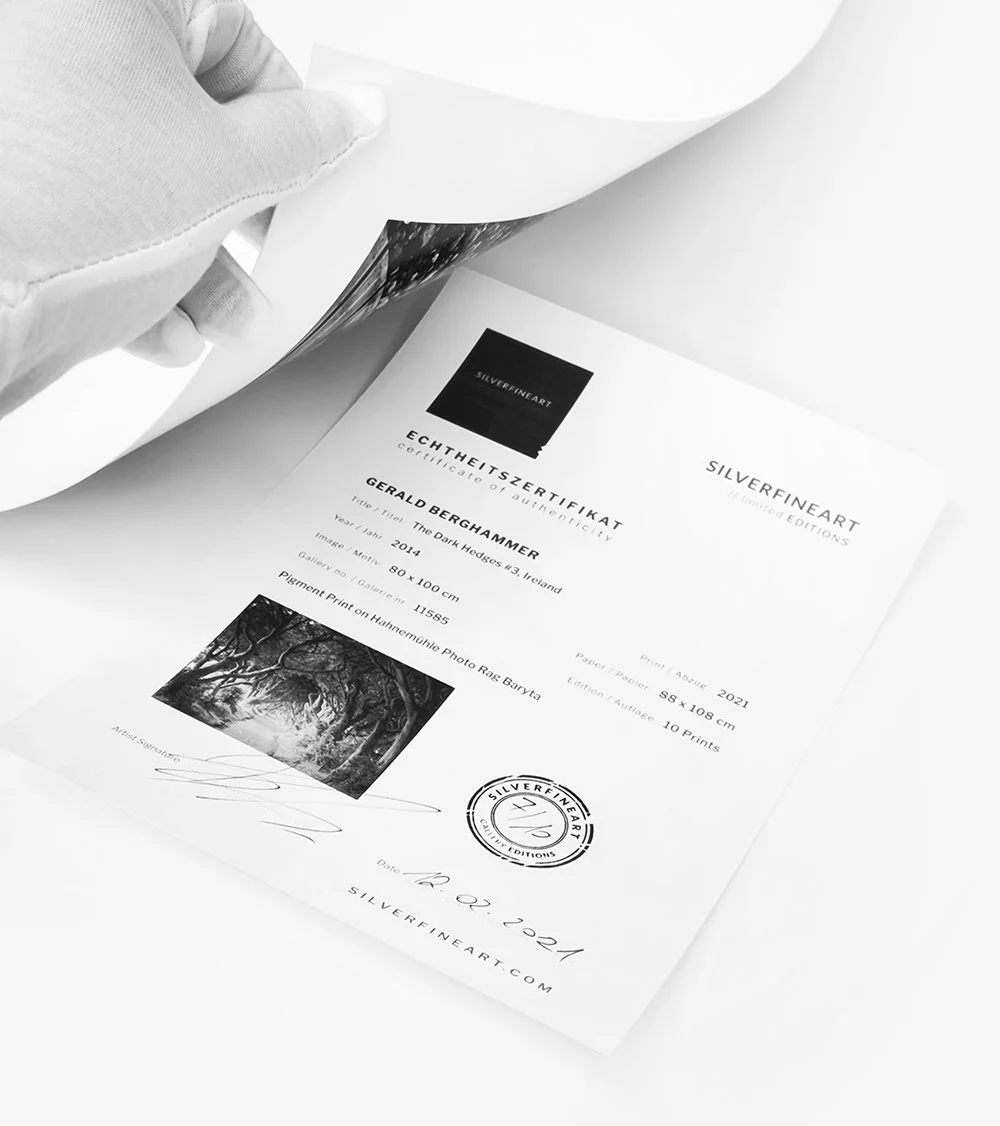 Gloved hand lifting a sheet to reveal a fine-art certificate of authenticity with artwork details, signature, and Silverfineart sea.