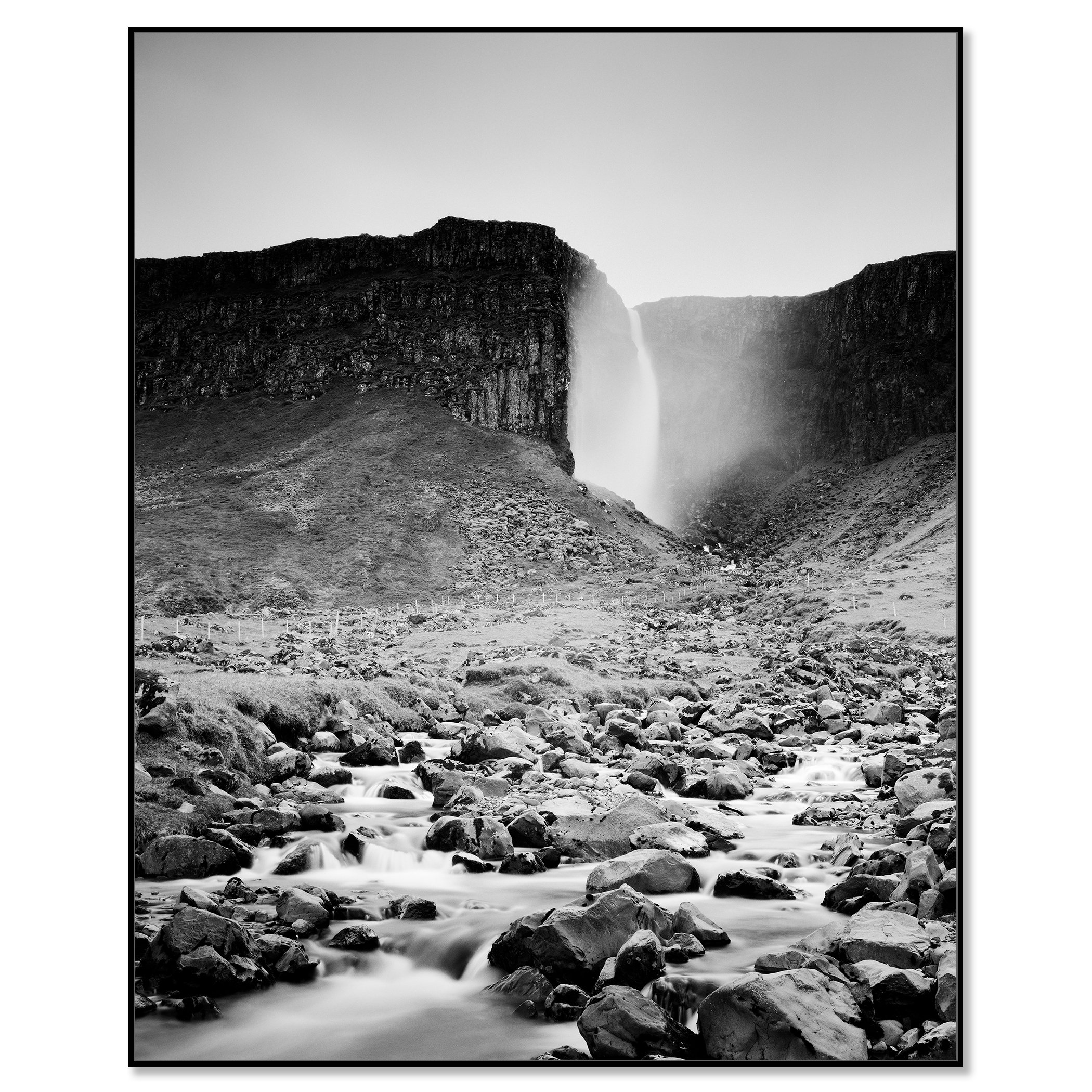 Gerald Berghammer - Black and white landscape photography. A waterfall cascading down a rocky cliff into a stream surrounded by rocks and rugged terrain. Chromaluxe framed black