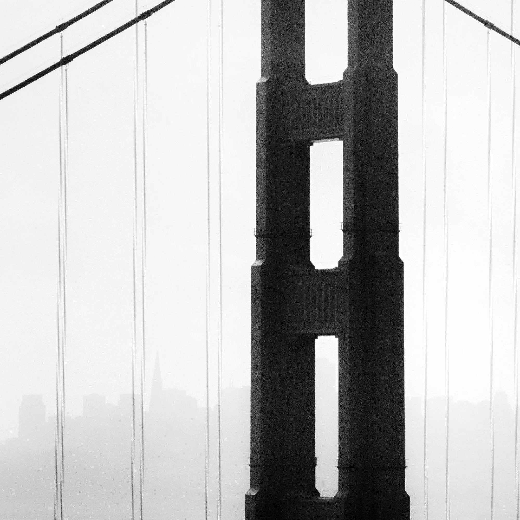 © 2015 Gerald Berghammer - Black and white photo. Golden Gate Bridge in San Francisco, seen from the side, with the city skyline faintly visible in the background. Print detail 1