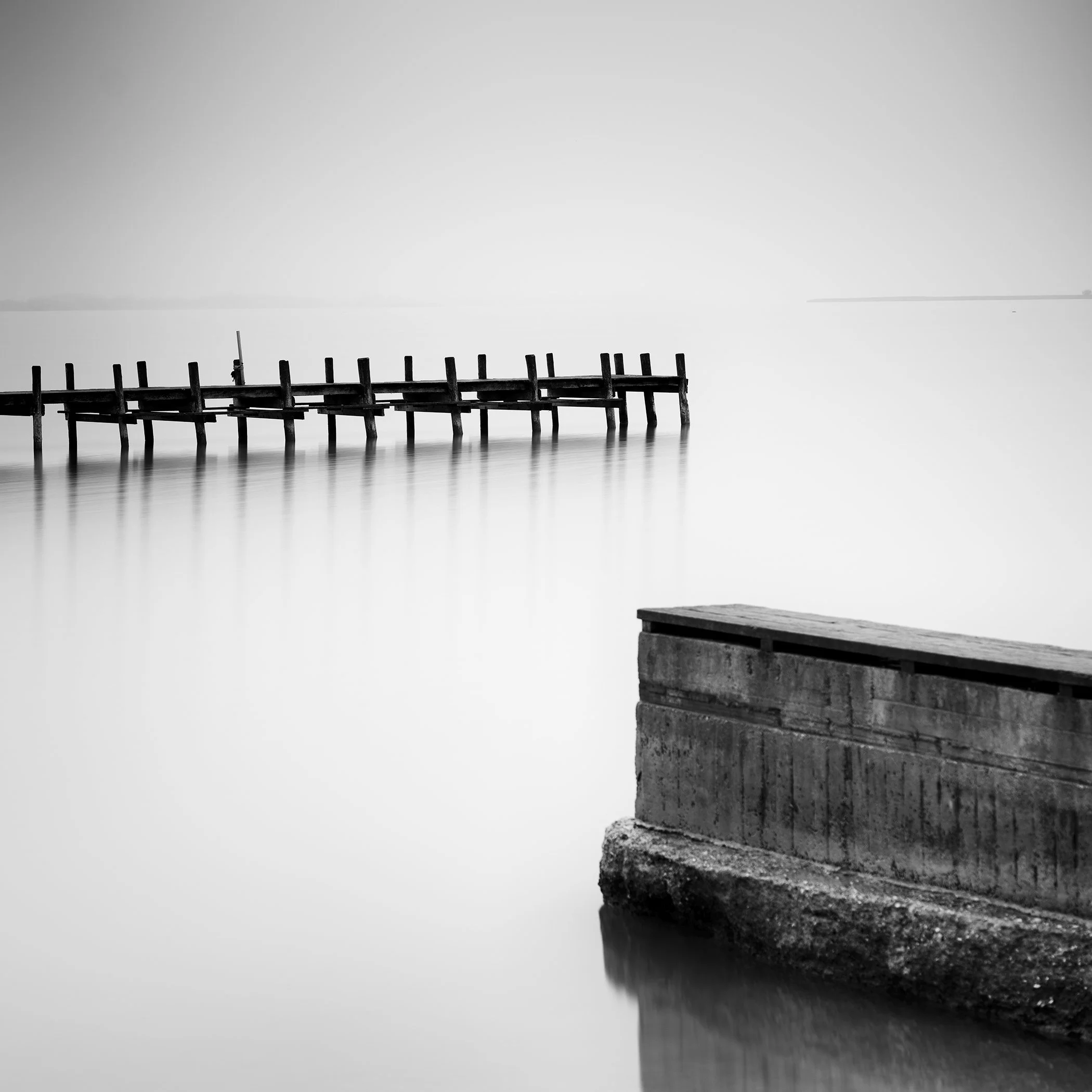 Black and white photo of a calm lake with an old wooden pier and concrete platform