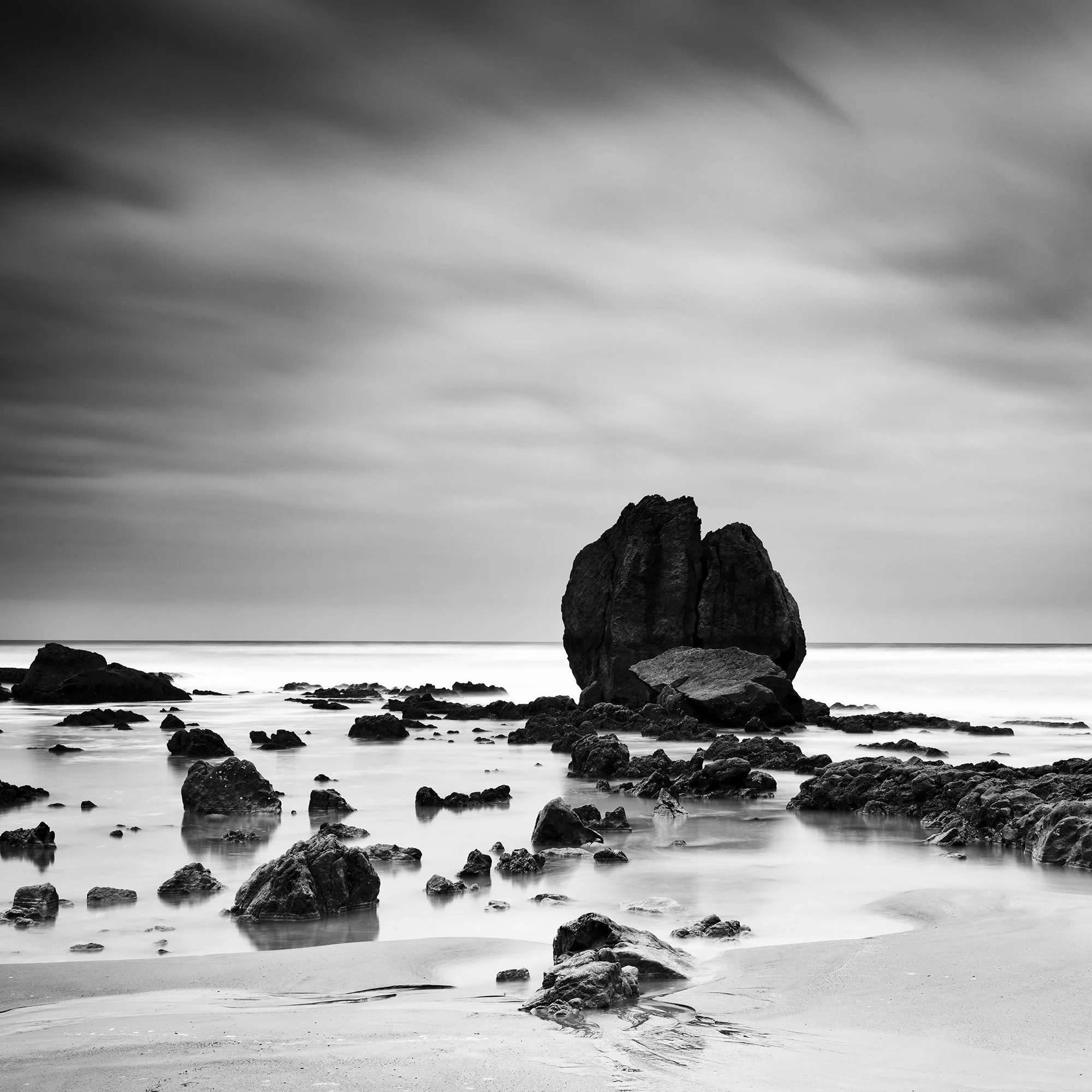 Rocks on the Shore Study 1 by Gerald Berghammer, black-and-white detail showing a monumental coastal rock surrounded by smaller formations and smooth water.