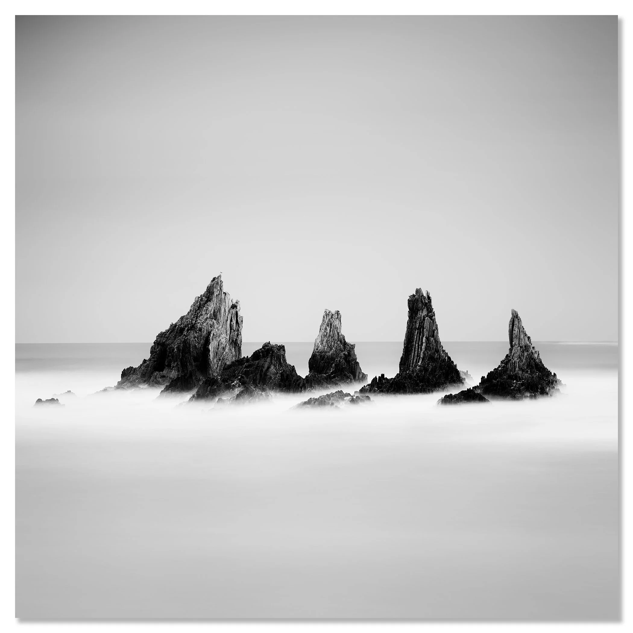 Black and white photograph of five jagged sea stacks rising from the Atlantic Ocean, with calm water and a clear sky – dibond frameless
