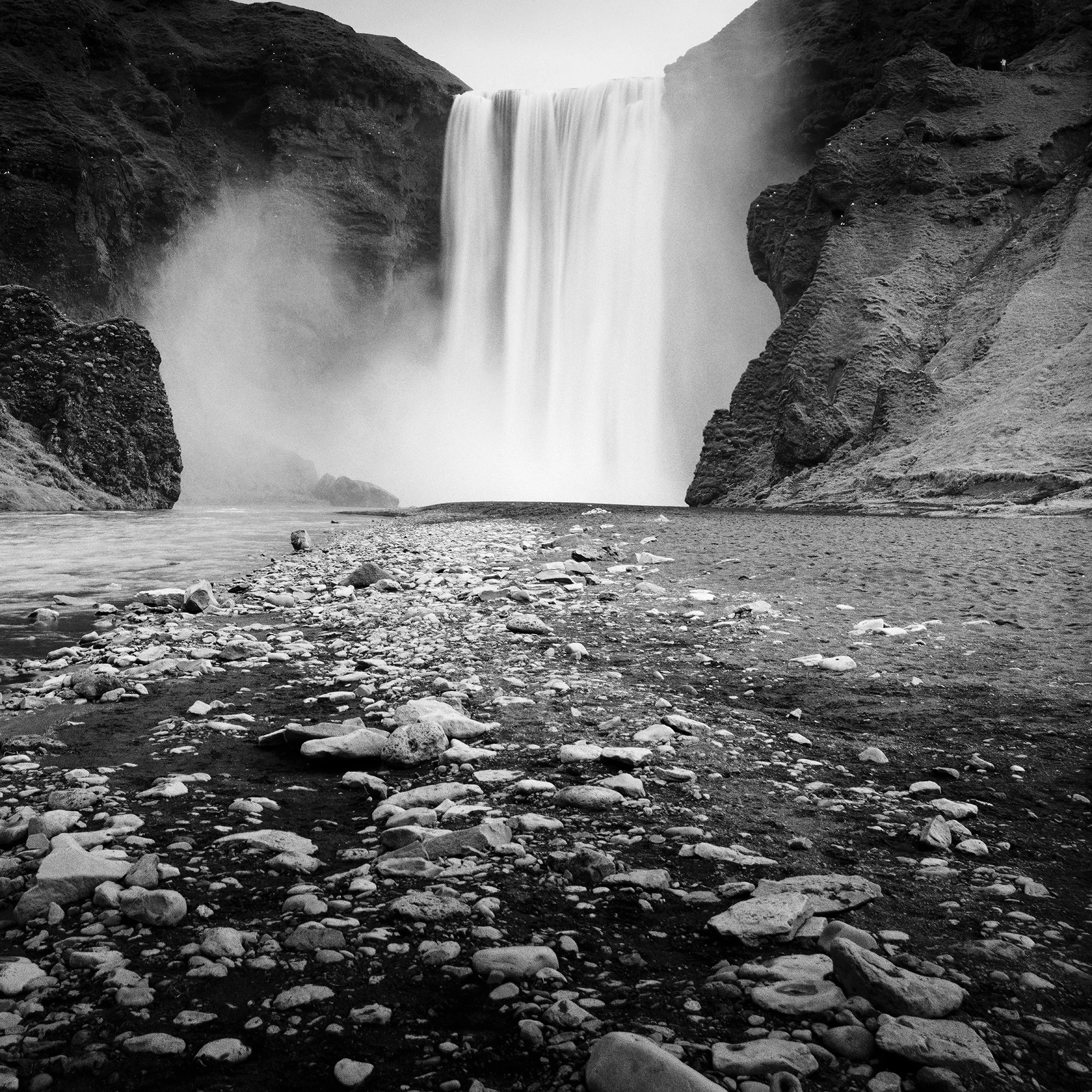 Gerald Berghammer - Black and white long exposure waterscape photography. A large waterfall flowing between rugged cliffs into a rocky river. Print detail 2