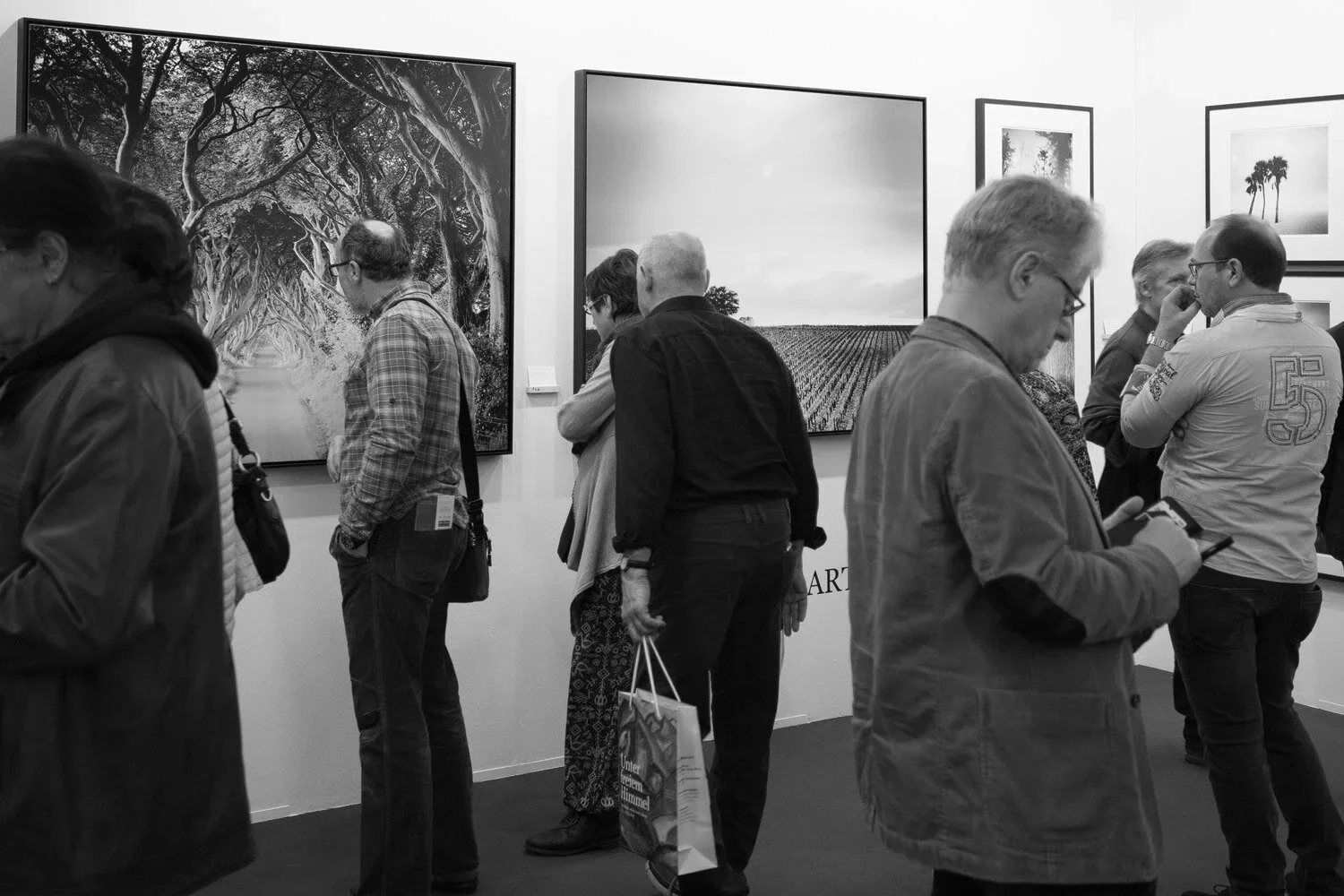 Visitors discussing framed black-and-white tree and landscape photographs by Gerald Berghammer at art KARLSRUHE 2017.
