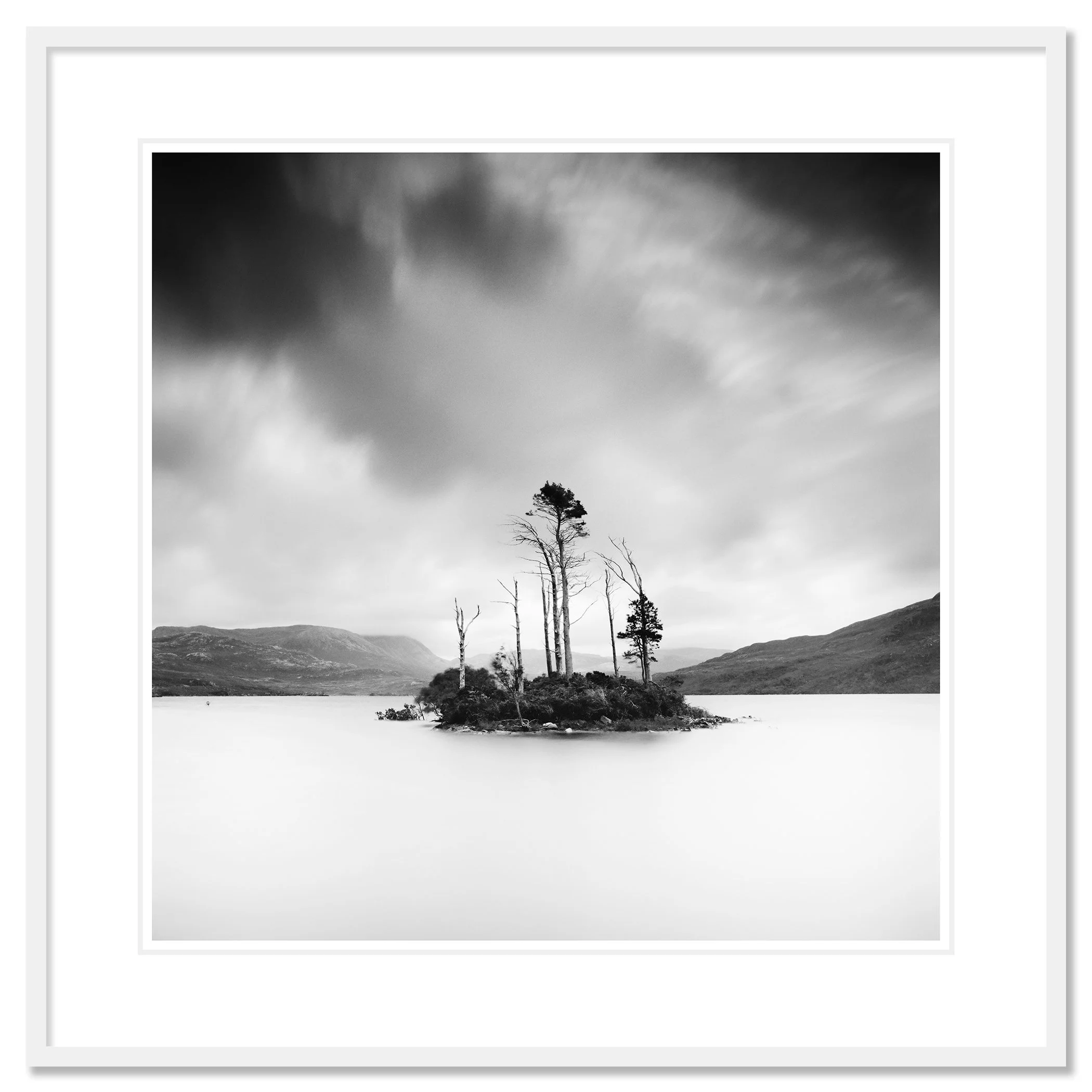 © 2012 Gerald Berghammer - Black and white waterscape photography. Small island with tall, thin trees surrounded by water and distant mountains under a cloudy sky. Classic framed white
