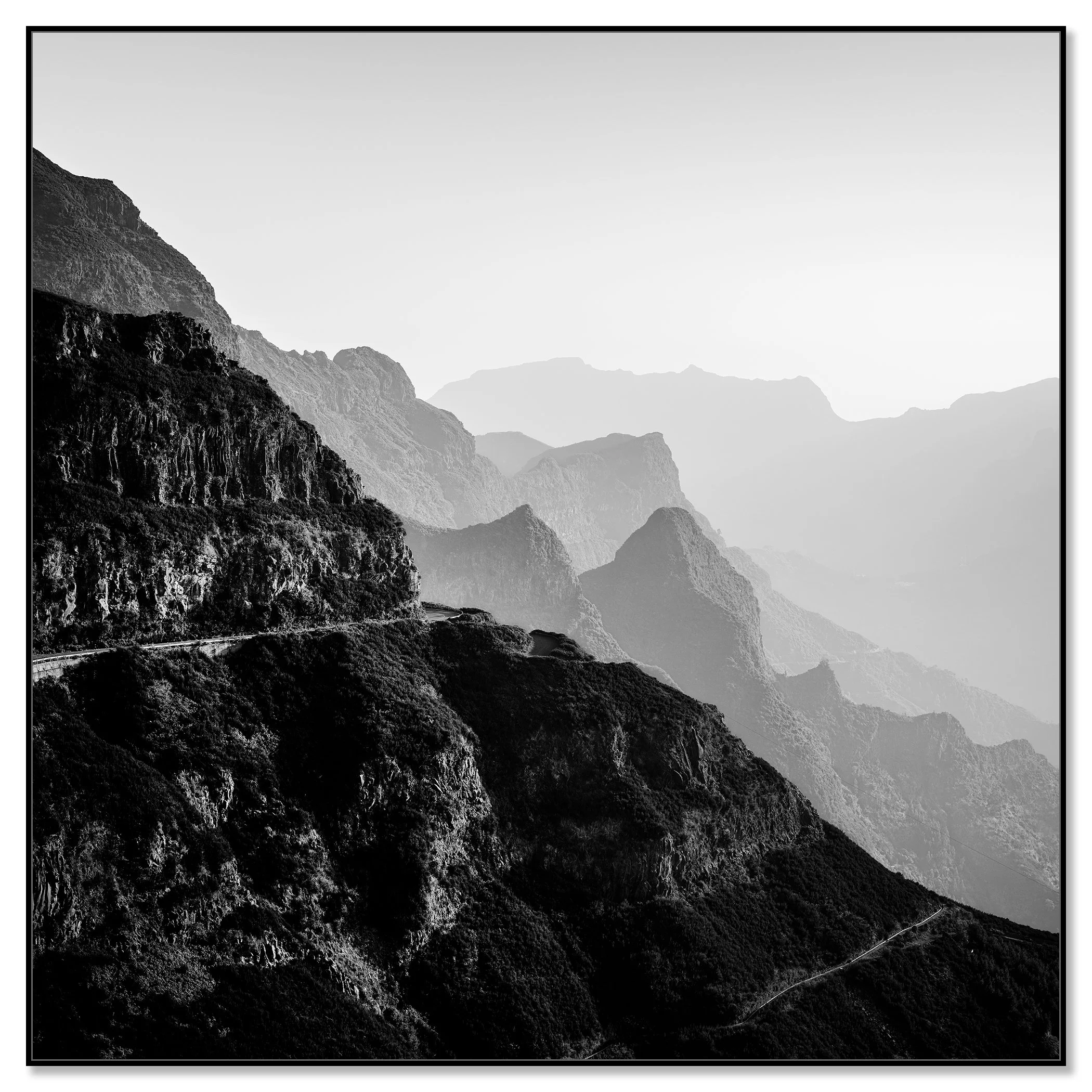 Black and white mountain landscape with rugged cliffs and a winding road in the haze – framed ArtBox black