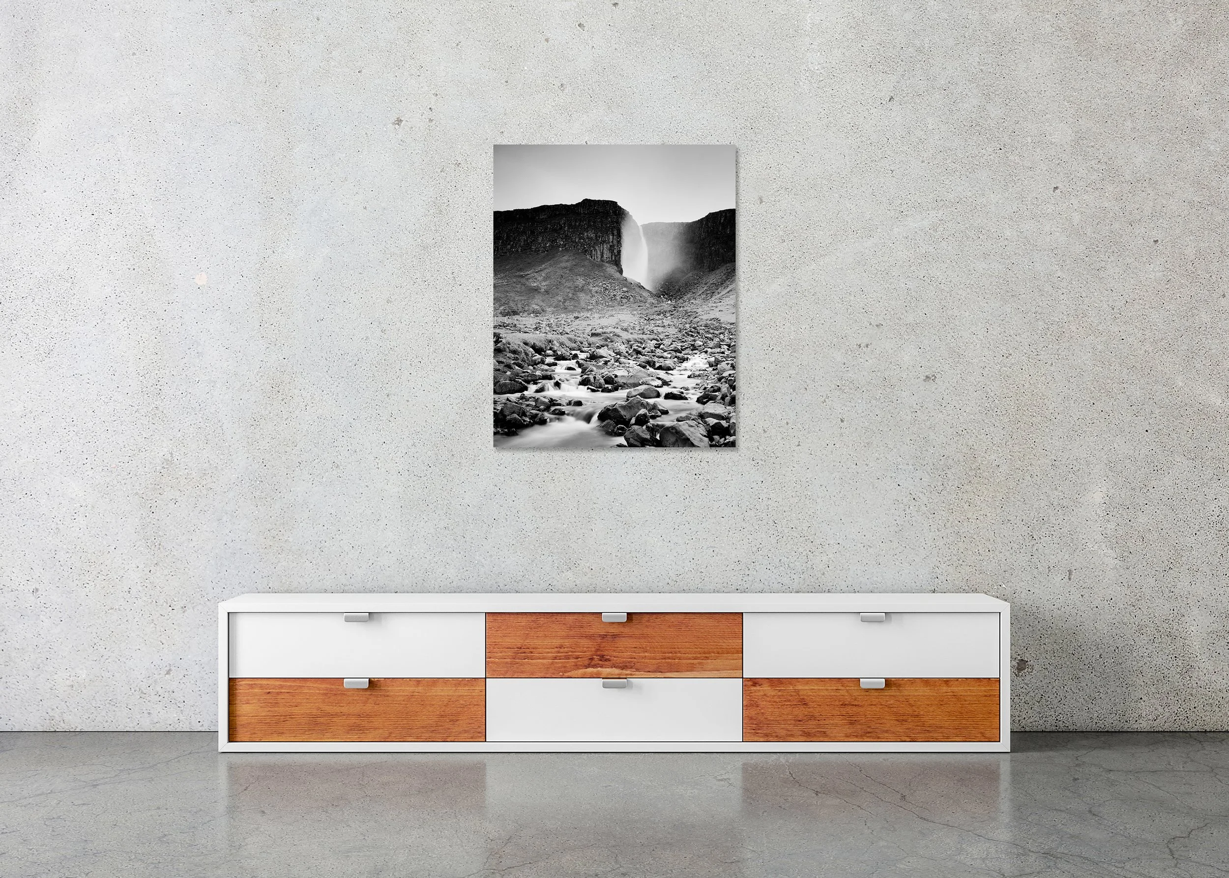 Monochrome landscape of an Icelandic waterfall between cliffs with misty spray and a rugged boulder-strewn riverbed, photo print mounted to Dibond, frameless.